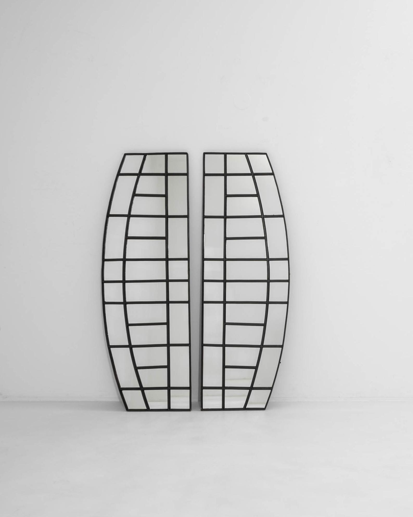 The unique design of this pair of vintage window mirrors makes an immediate impression. Made in France in the 20th century, the interplay of broad curves and straight lines creates a striking geometry, emphasized by the graphic bars of the dark iron
