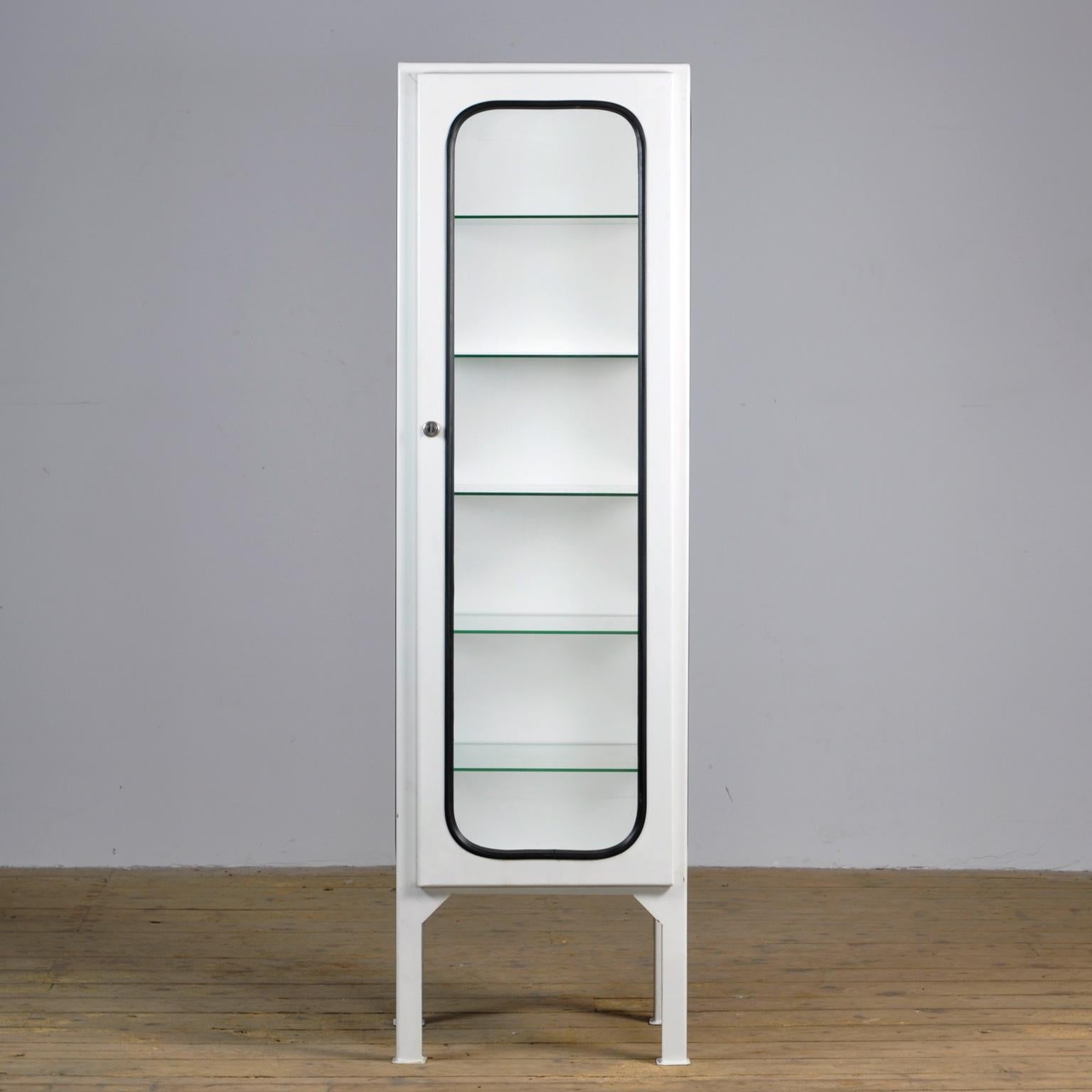 This medicine cabinet was designed in the 1970s and produced in 1975, in Hungary. It is made from steel and glass, with the glass panes held in place by a black rubber strip. The cabinet features five adjustable glass shelves and a functioning lock.