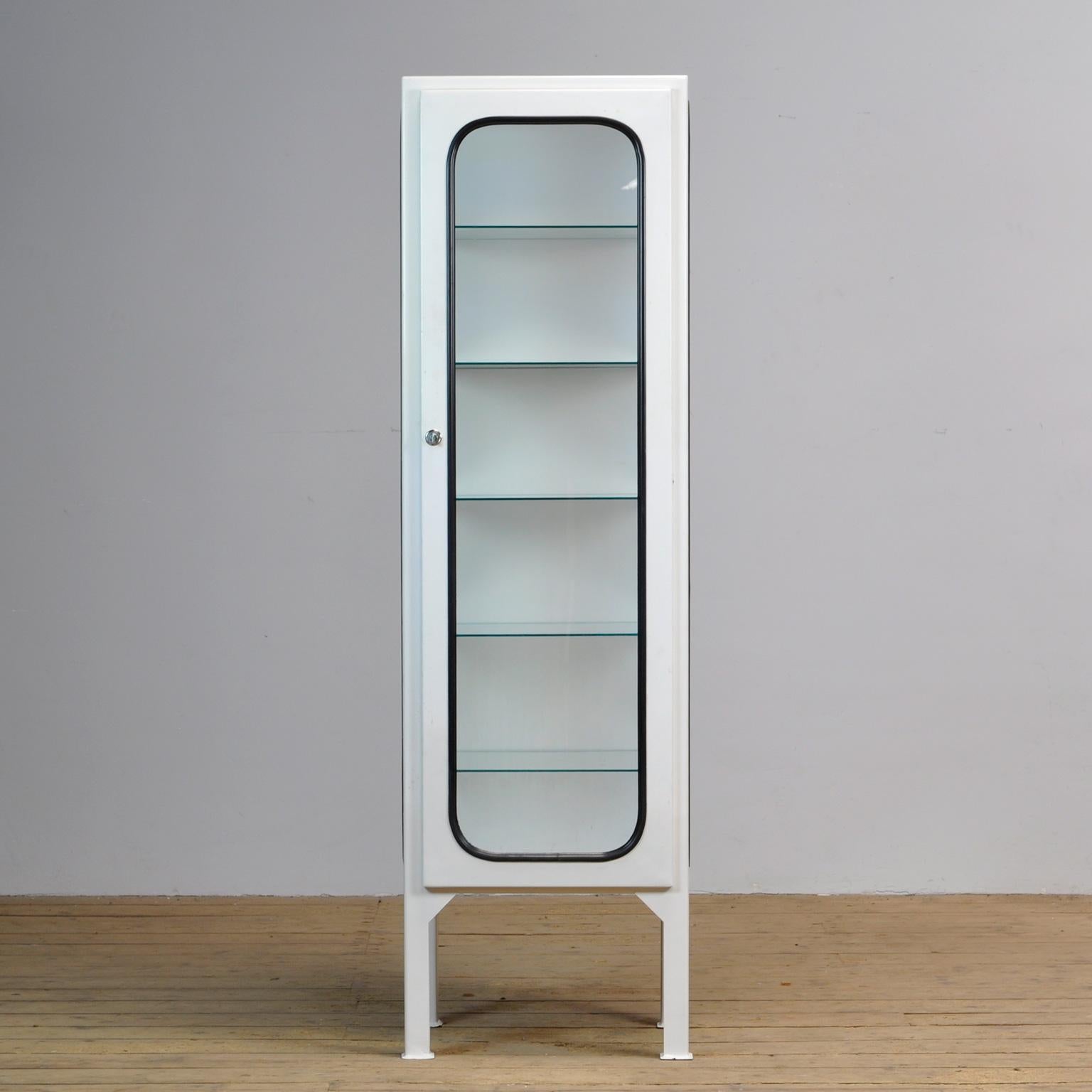 This medicial cabinet was designed in the 1970s and produced in 1975 in hungary. It is made from steel and glass, the glass is held in place by a black rubber strip. The cabinet features five adjustable glass shelves and a functioning lock/key.