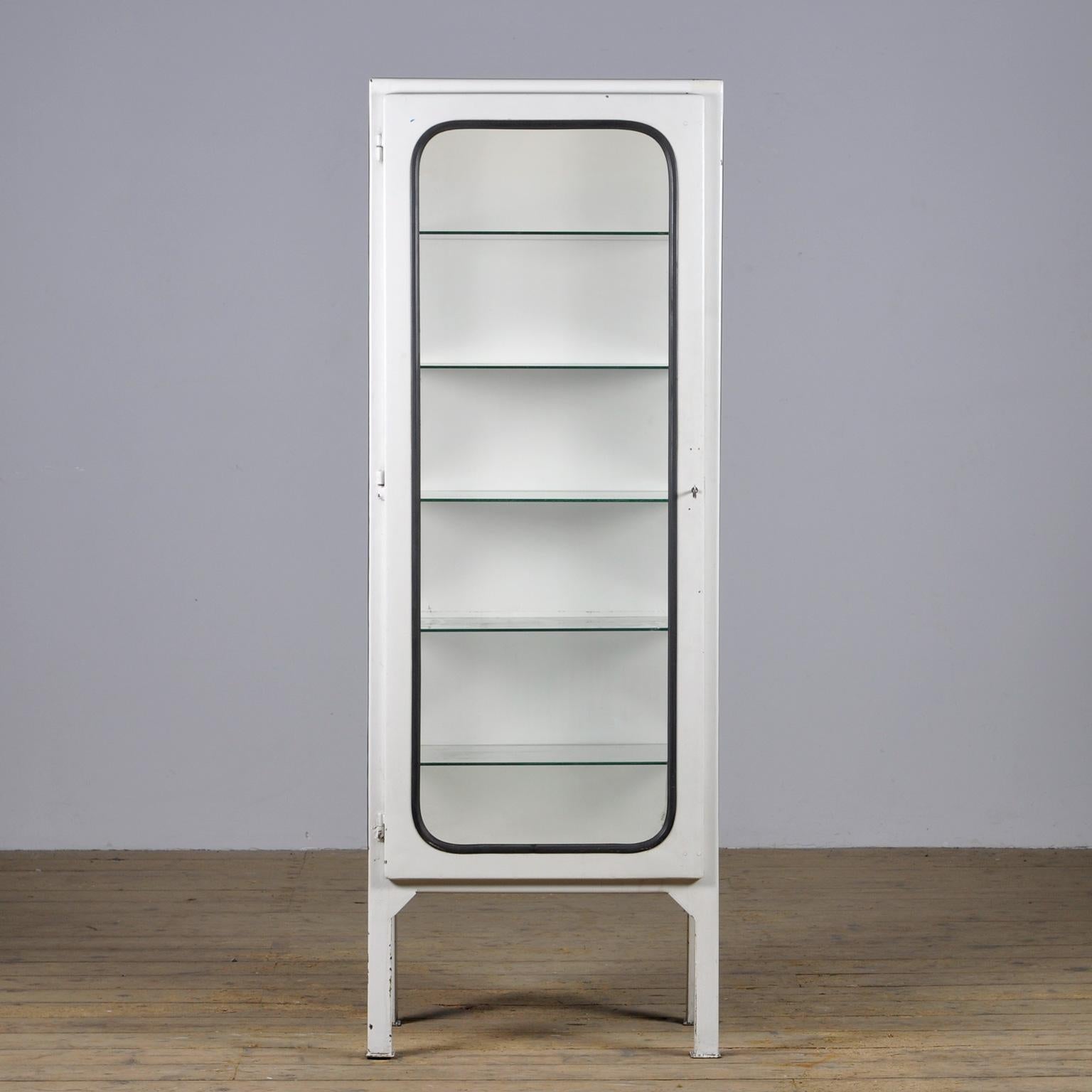 This medical cabinet was designed in the 1970s and produced in 1975 in hungary. It is made from steel and antique glass, the glass is held in place by a black rubber strip. The cabinet features five adjustable glass shelves and a functioning