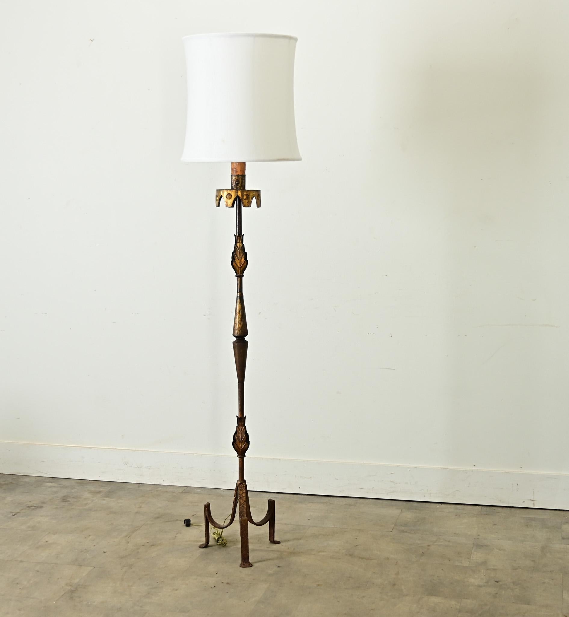 Vintage midcentury Spanish wrought iron floor lamp circa 1950, a sculptural piece that features stylized leaf decorations on the thin pole, supported by a tripod base. Parcel gilt adds a touch of flamboyance to the already creative design, which