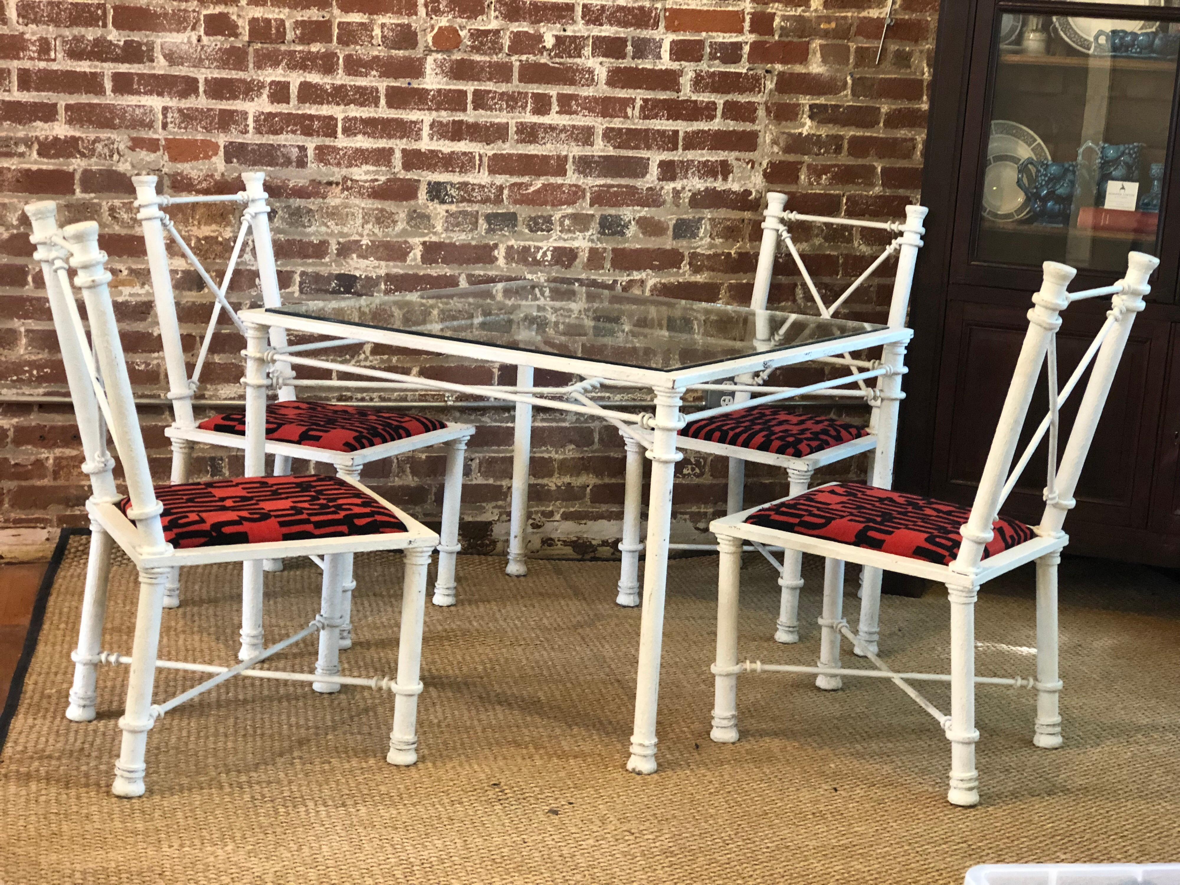 A vintage iron garden or patio set having a square glass top table and four chairs. The table and chairs have a rustic white paint finish and unusual decorative neoclassical faux rope ties as stretchers. The table measures 40 inches square by 28.75