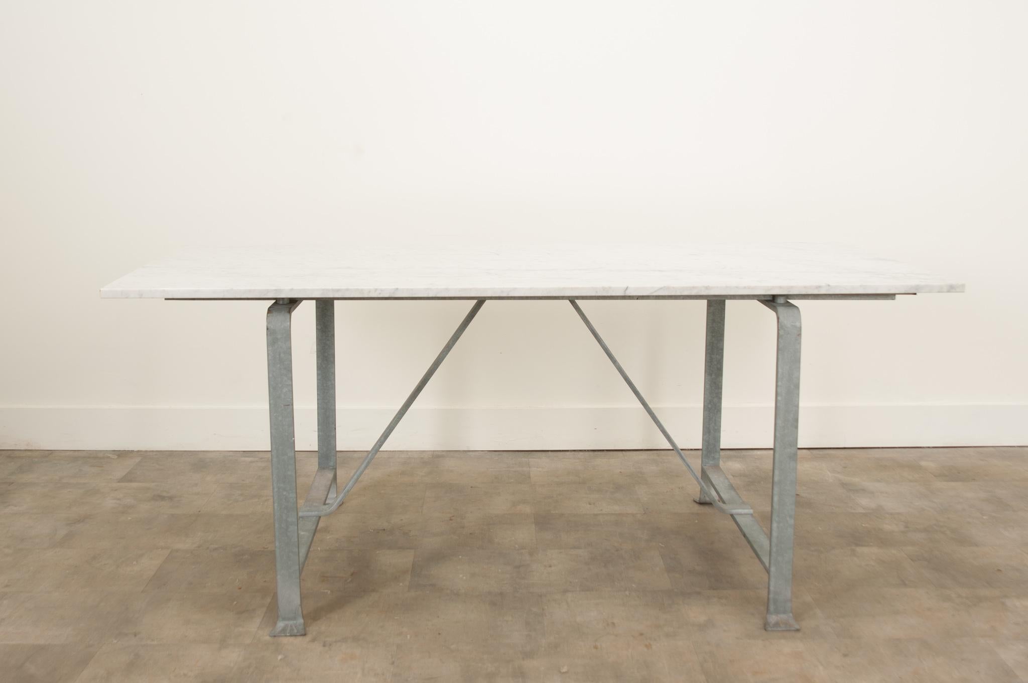 A vintage English iron dining table with a white marble top hand made in England circa 1900’s. The table is raised by an attractive wrought iron base with a lovely gunmetal gray finish and features elegant lines, a connecting stretcher for