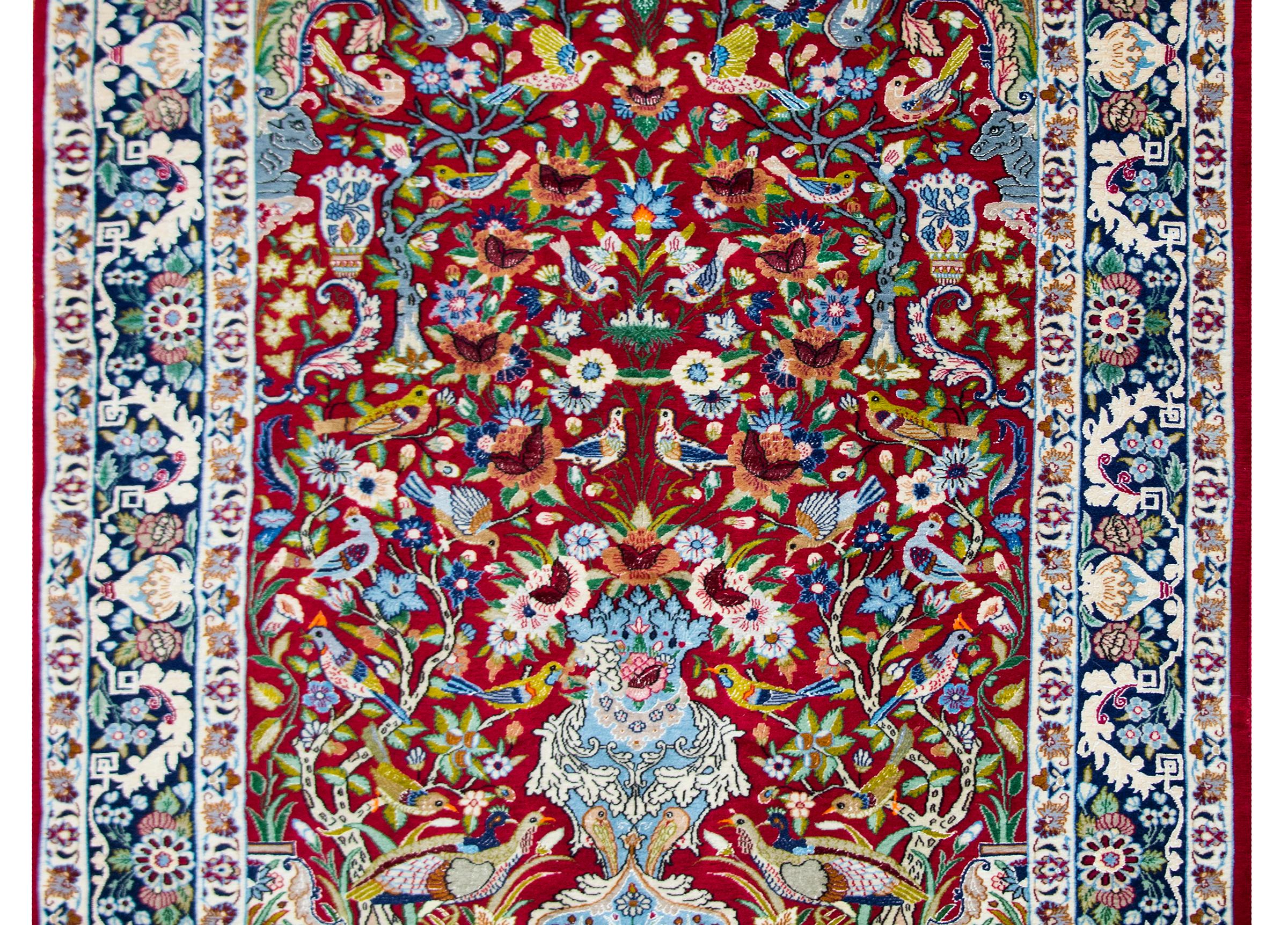 A wonderful late 20th century Persian Isfahan rug with a large central vase sprouting a tree-of-life with myriad flowers and birds, surrounded by a wide border with a large floral and leaf pattern flanked by pairs of thinner floral partnered