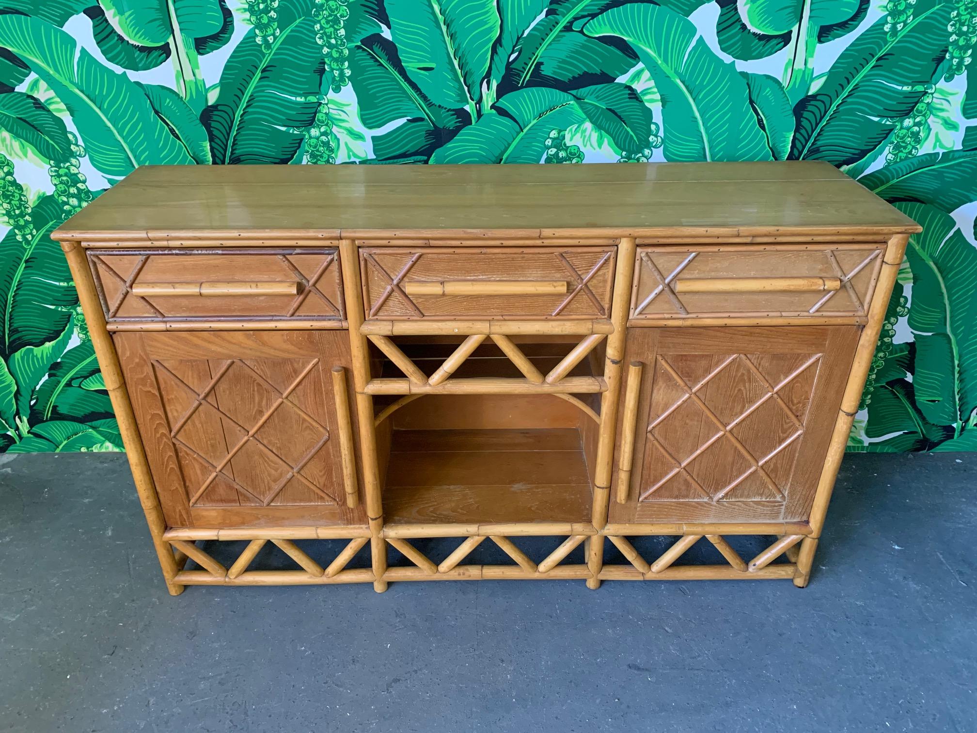 Rattan server circa 1960s features three drawers, two doors revealing shelved storage, and a unique curved center shelf. Rattan skirt and door faces in a cross hatch pattern. Good vintage condition with minor imperfections consistent with age.