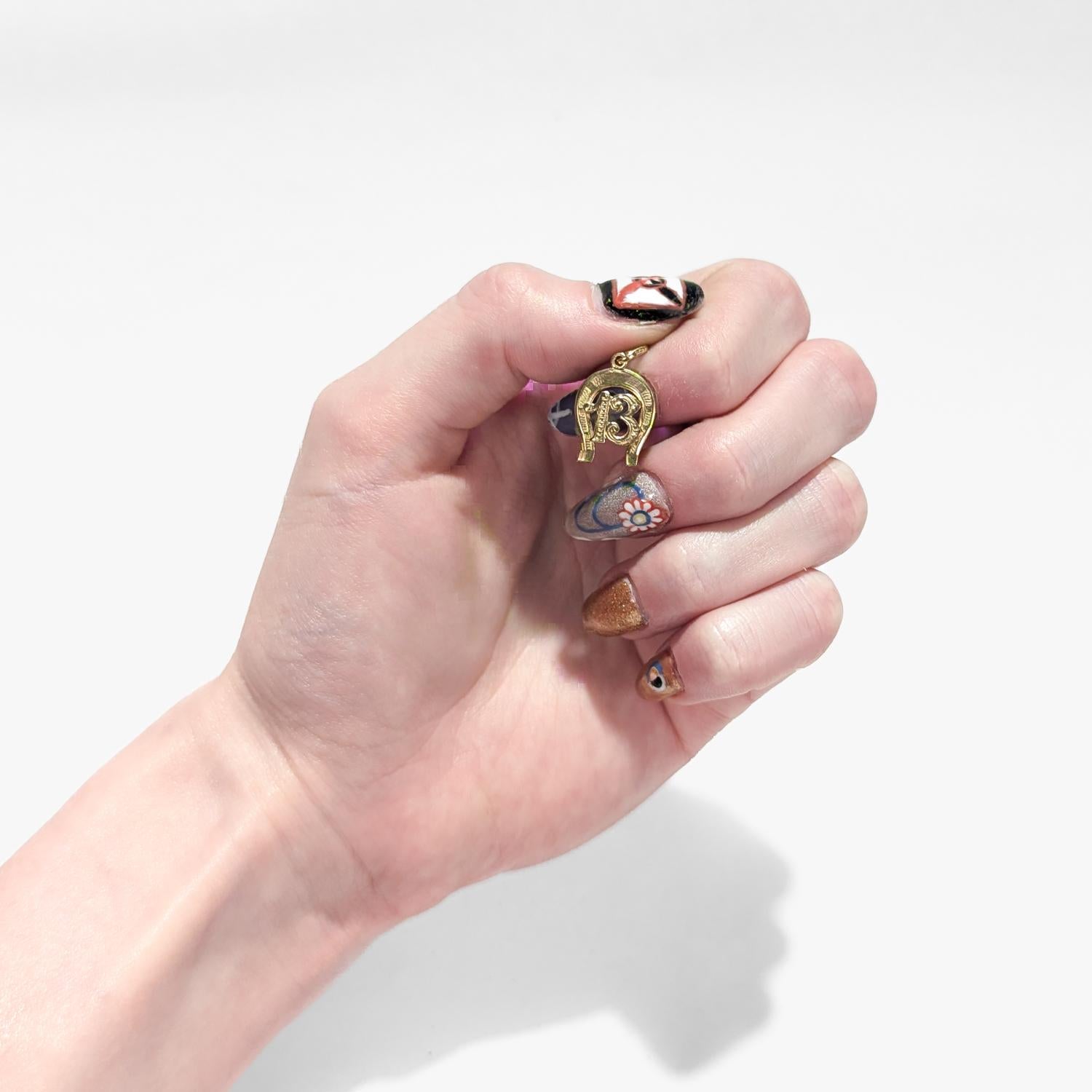 A fine vintage Italian gold charm or pendant.

In 14 karat yellow gold.

In the form of a horseshoe with the number 13 at its center. 

13 is considered lucky in Italian culture - in large part because the football betting pool Totocalcio allowed a