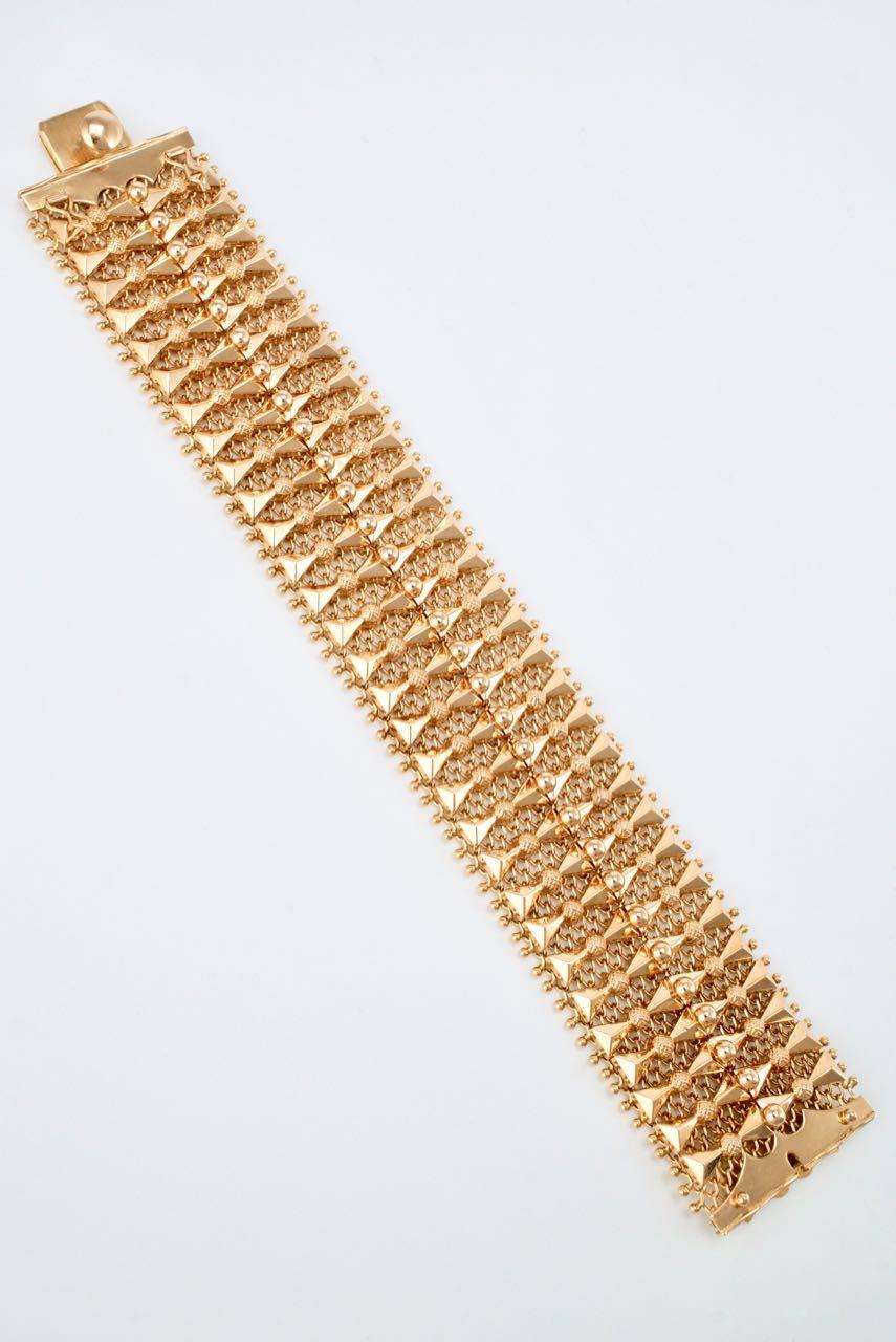 An 18 karat yellow gold wide bracelet of triangular motifs with textured and polished bead spacers mounted on a fine mesh backing with integrated box clasp closure and double figure of eight safety clasps - a bold but delicate design in a lovely