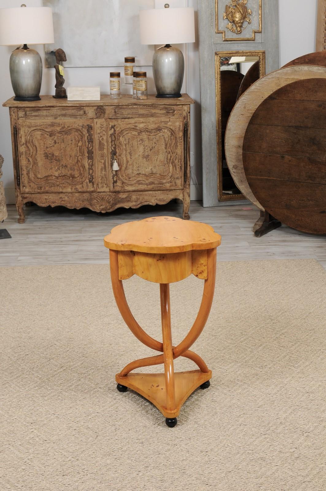 An Italian vintage burl wood guéridon side table with clover-shaped top, single serpentine drawer, intertwined base with lower shelf and ebonized wooden feet from the first half of the 20th century. The perfect sized side table in a graceful and