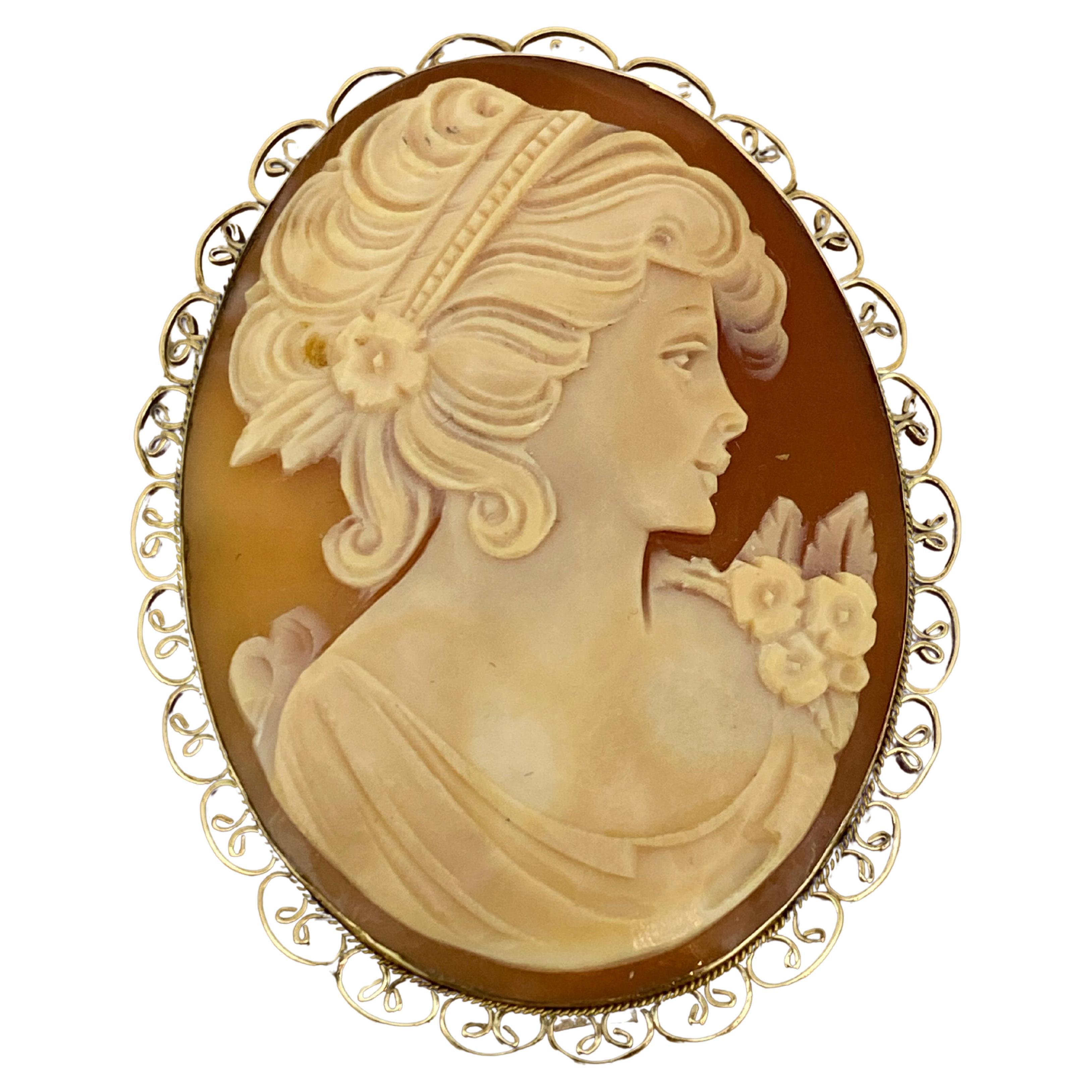 Cette broche vintage en forme de camée en coquillage finement sculpté 
représente le profil d'une jeune femme, 
incroyablement détaillé, 
dans une bordure décorative en or jaune 9K finement détaillée 

Il est muni d'une épingle et d'une attache -