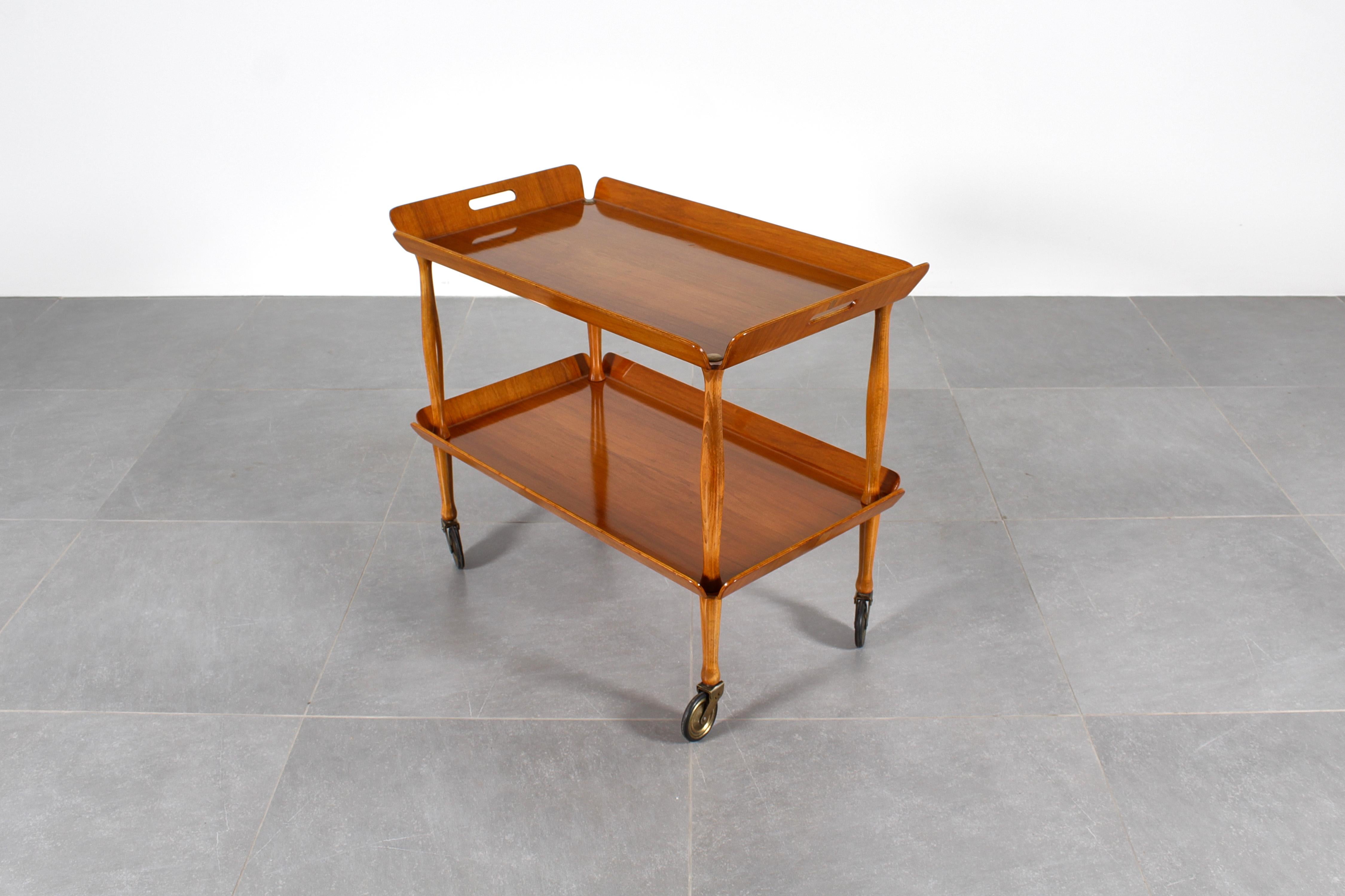 Chariot de service élégant et restauré avec double étagère en contreplaqué repliée sur les côtés, avec roues et finitions en laiton. Production italienne des années 1950.
Usure conforme à l'âge et à l'utilisation.