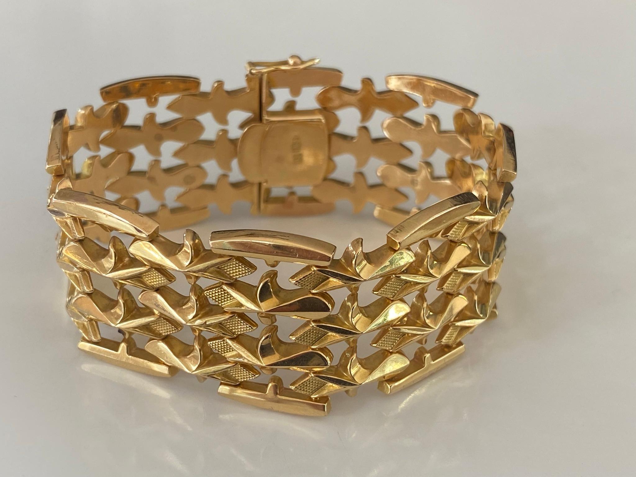 Ce magnifique bracelet à maillons repoussés, fabriqué à la main en or jaune 18 carats, présente un motif répétitif de fleurs de lys dans un design ajouré à quatre rangs. Fabriquées en Italie.  Le bracelet mesure 6,85 pouces et 1,15 pouce (26 mm) de