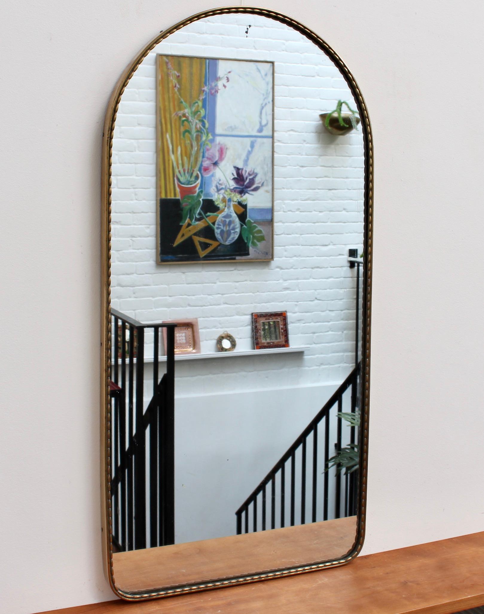 Vintage Italian arch-shaped wall mirror with brass frame and distinctive beading (circa 1950s). The mirror has both a ruggedness and elegant good looks all at once. It is in overall fair vintage condition presenting an aged patina with characterful