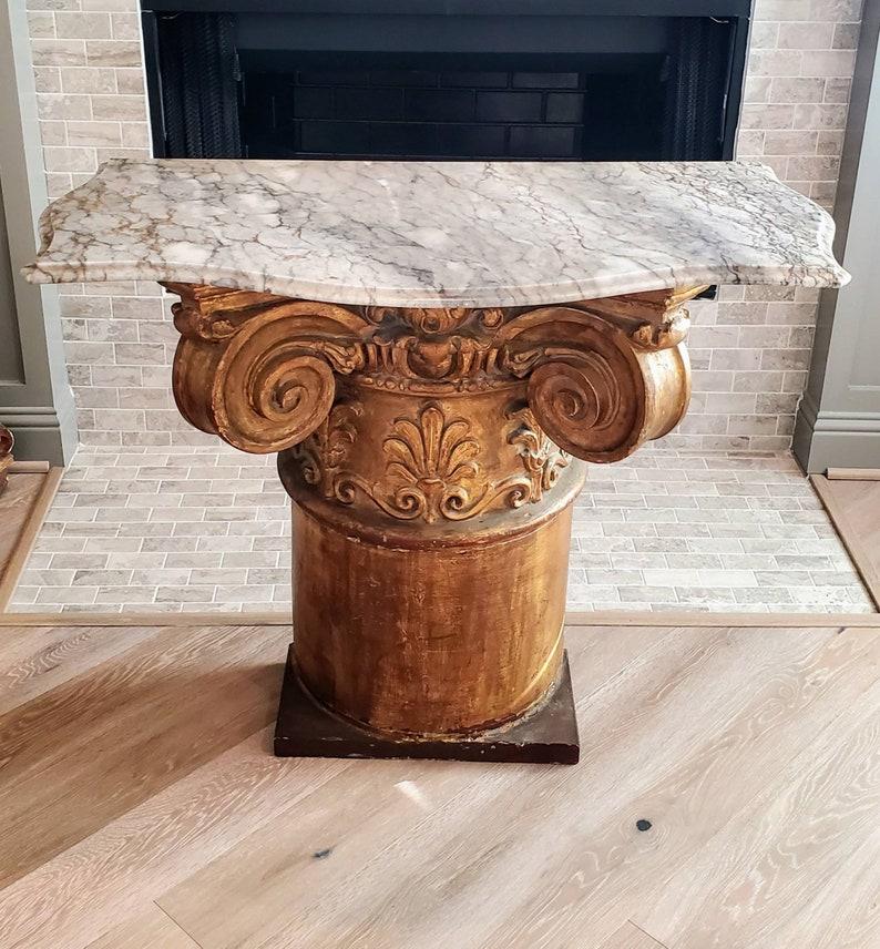 A vintage Italian decorative architectural gilt Neoclassical corinthian capital column repurposed into a console table, with striking serpentine shaped ogee molded edge richly veined gray marble top, atop the hollowed ceramic demilune pedestal