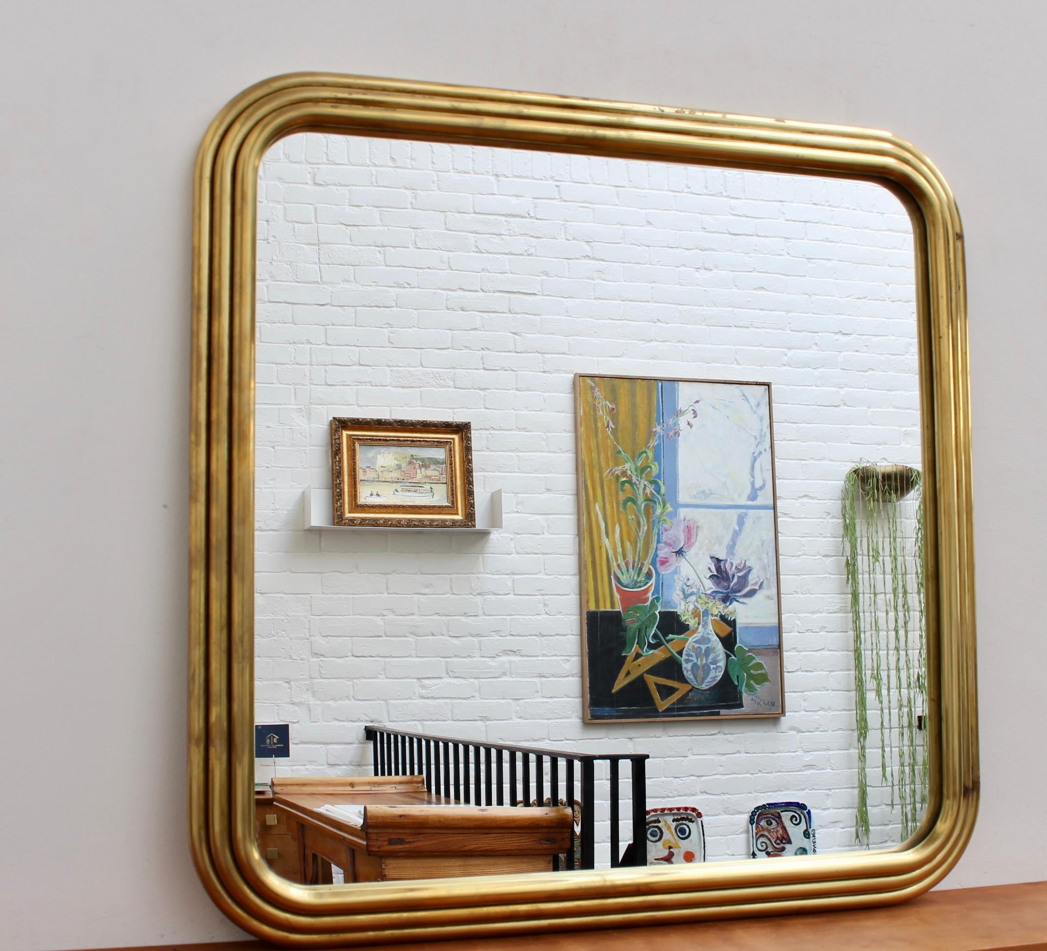 Italienischer Art-Déco-Wandspiegel aus der Mitte des Jahrhunderts mit Messingrahmen (ca. 1960er Jahre). Der Spiegel ist quadratisch mit sinnlich geschwungenen Rändern und einem Art-Déco-Rahmen mit sich wiederholendem Rohrmotivrahmen. Sehr elegant