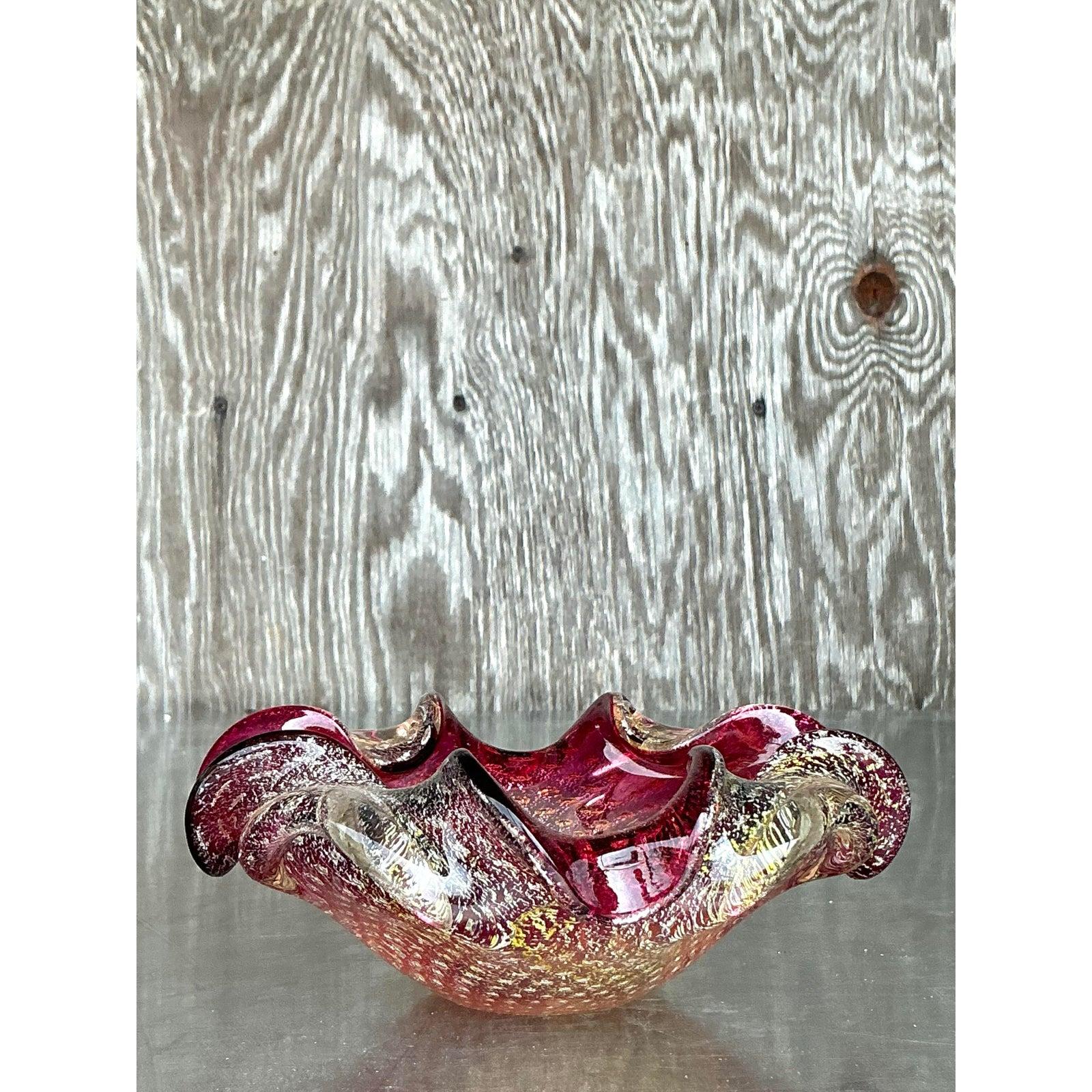 Add a pop of color and craftsmanship to your decor with this exquisite vintage Italian art glass bowl, styled after iconic Murano glassmaking techniques. With its rich ruby red hues, gold and silver flecks, and organically ruffled edges, this