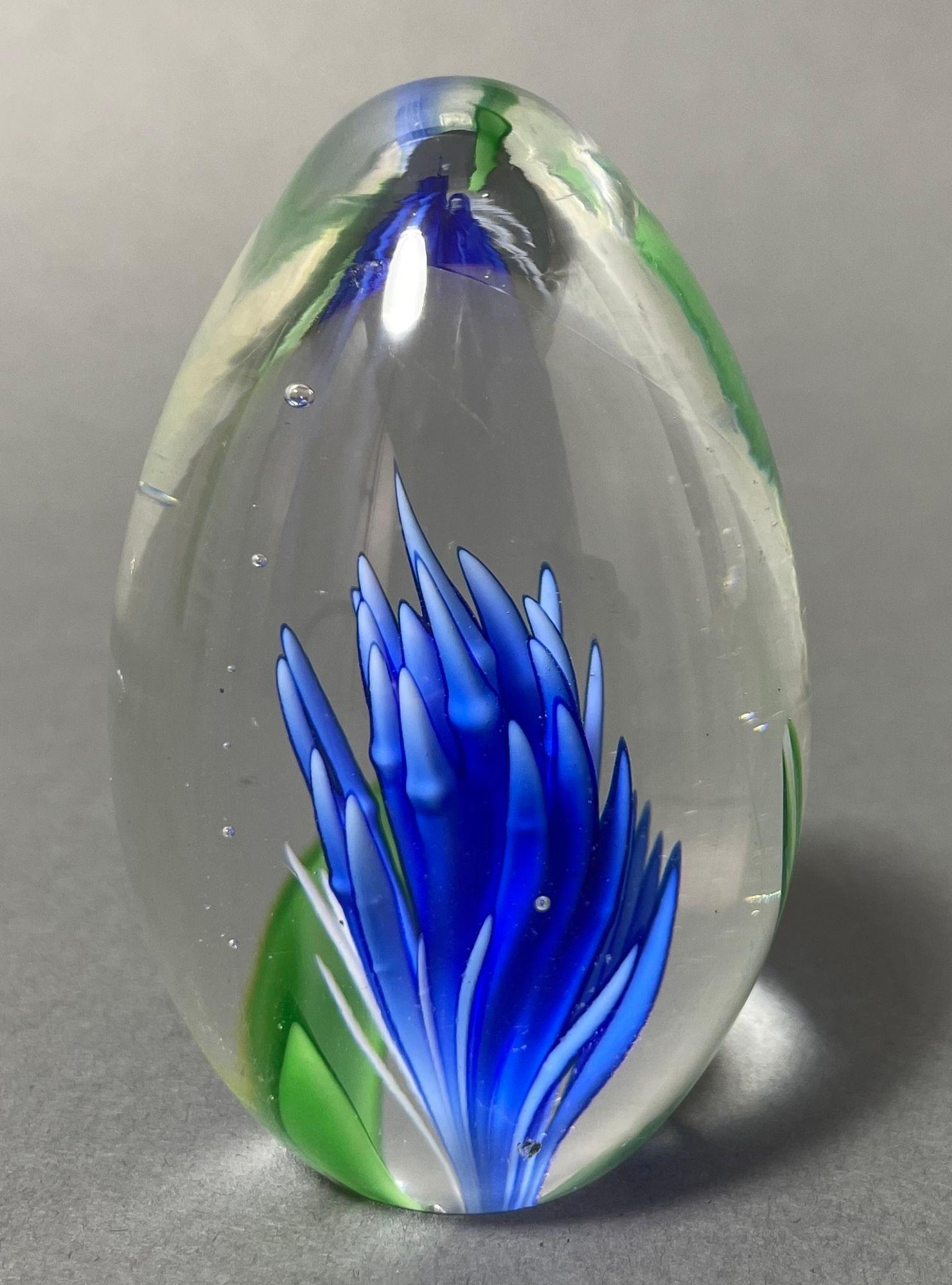 Vintage Italian blown art glass paperweight in vibrant blue and green in a transparent egg shape.
Vintage Italian Murano Hand blown art glass egg shaped paperweight, with encased bright blue glowing underwater plant with green oceanic leaves in