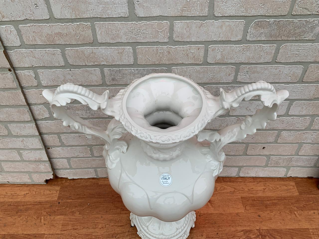 Vaso di Capodimonte bianco dei fratelli Azzolin d'epoca con maniglie

Decora il tuo tavolino con questo vaso monocromatico in ceramica bianca. Il vaso è costruito in modo ornamentale con ampi manici fioriti e una base ondulata. Come indicato