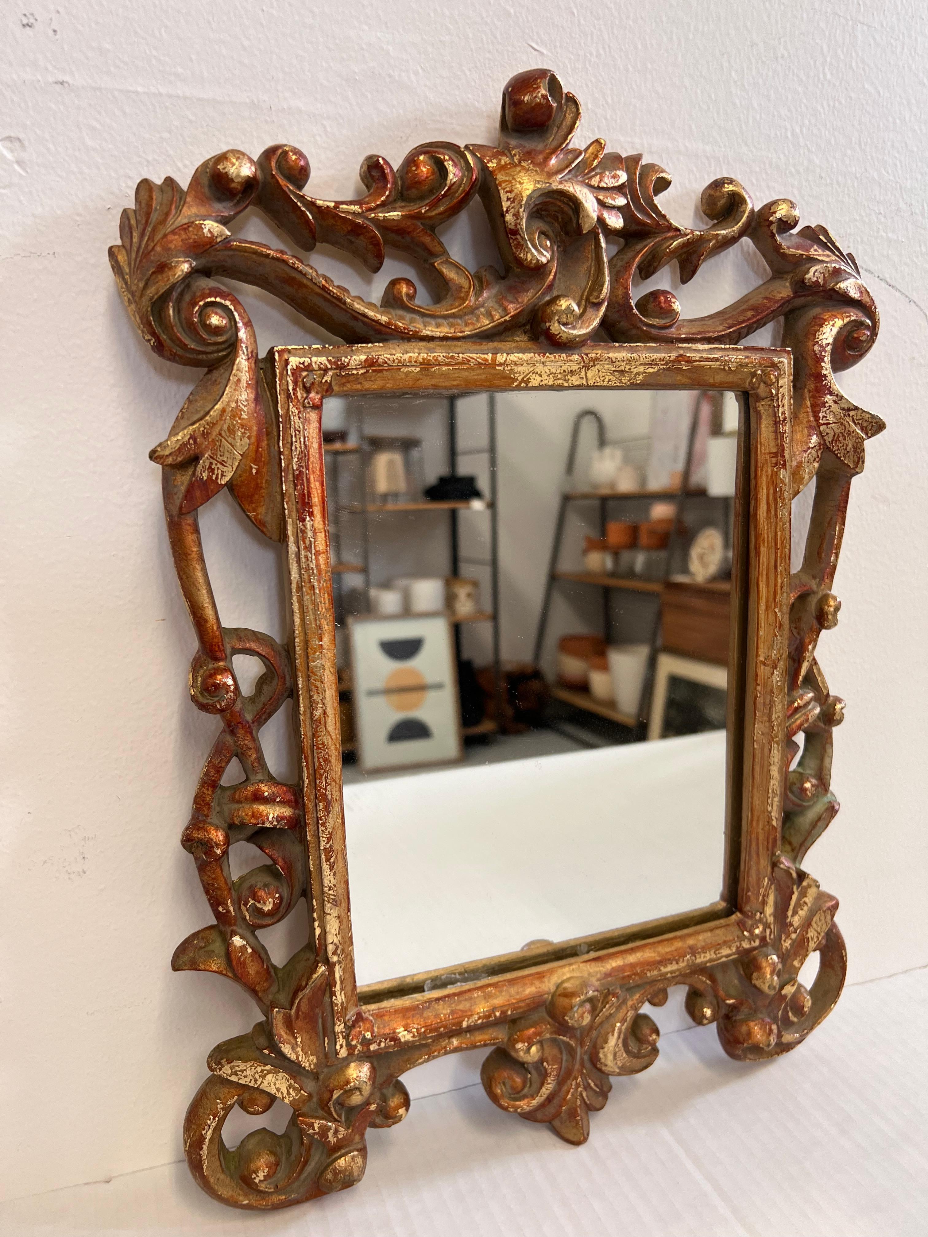 Questo specchio in legno dorato in stile barocco italiano presenta una cornice ornata da intricati intagli e abbellimenti tipici del periodo barocco. La cornice è ornata da elaborate volute, motivi di foglie e una cresta decorativa superiore, che