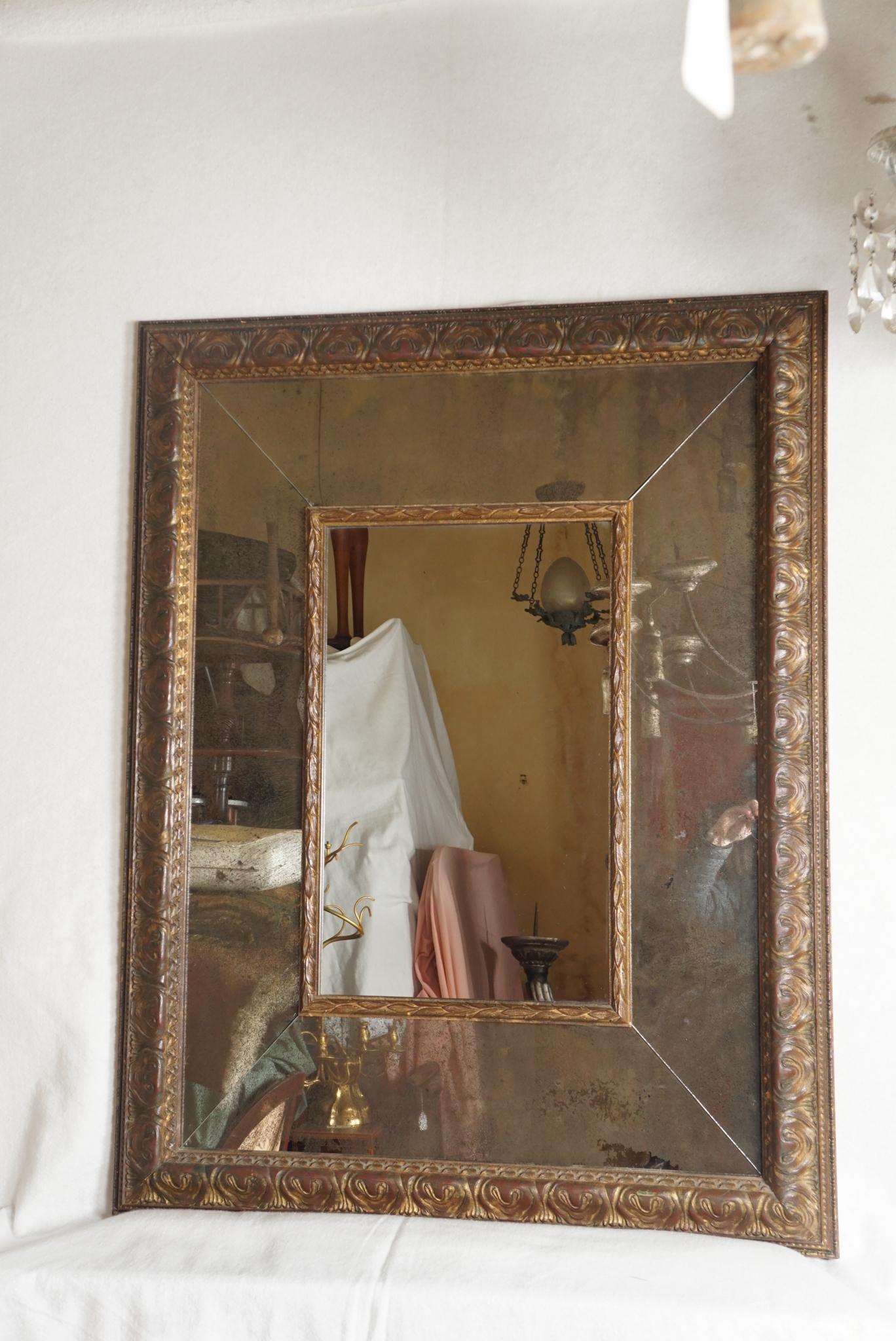 Fabriqué vers 1950, ce miroir vintage en bois sculpté présente une surface et un style anciens. La dorure Florentine est riche étant posée sur un fond rouge profond donnant ainsi au frottement vie et mouvement. Le cadre est constitué d'un large