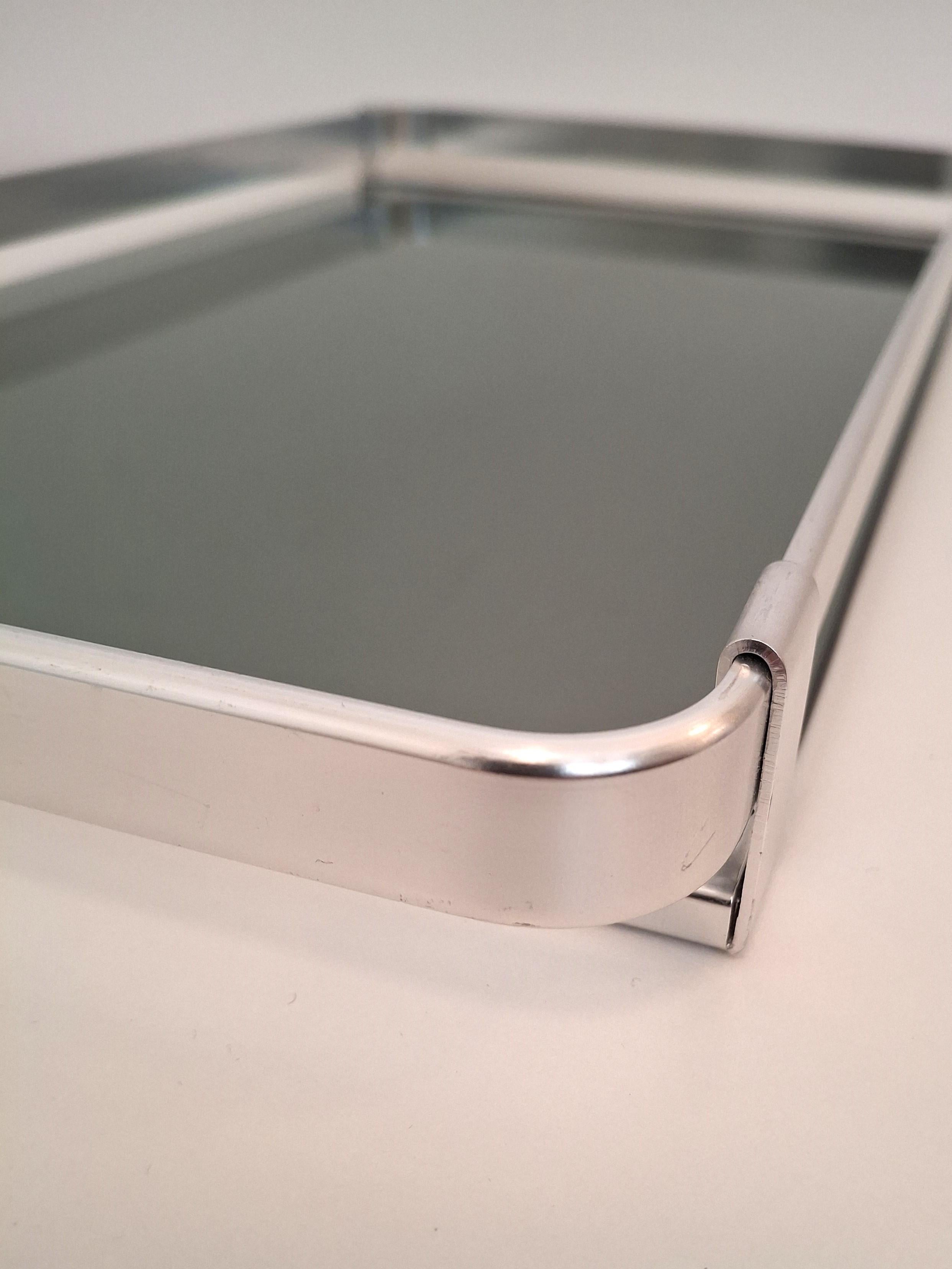 Mit diesem exklusiven Serviertablett im Bauhaus-Stil, das in den 1970er Jahren in Italien hergestellt wurde, werten Sie Ihren Raum auf. Mit seinem eleganten Metallrahmen und dem Rauchglas ist dieses Tablett ein wahrer Augenschmaus. Die glatten