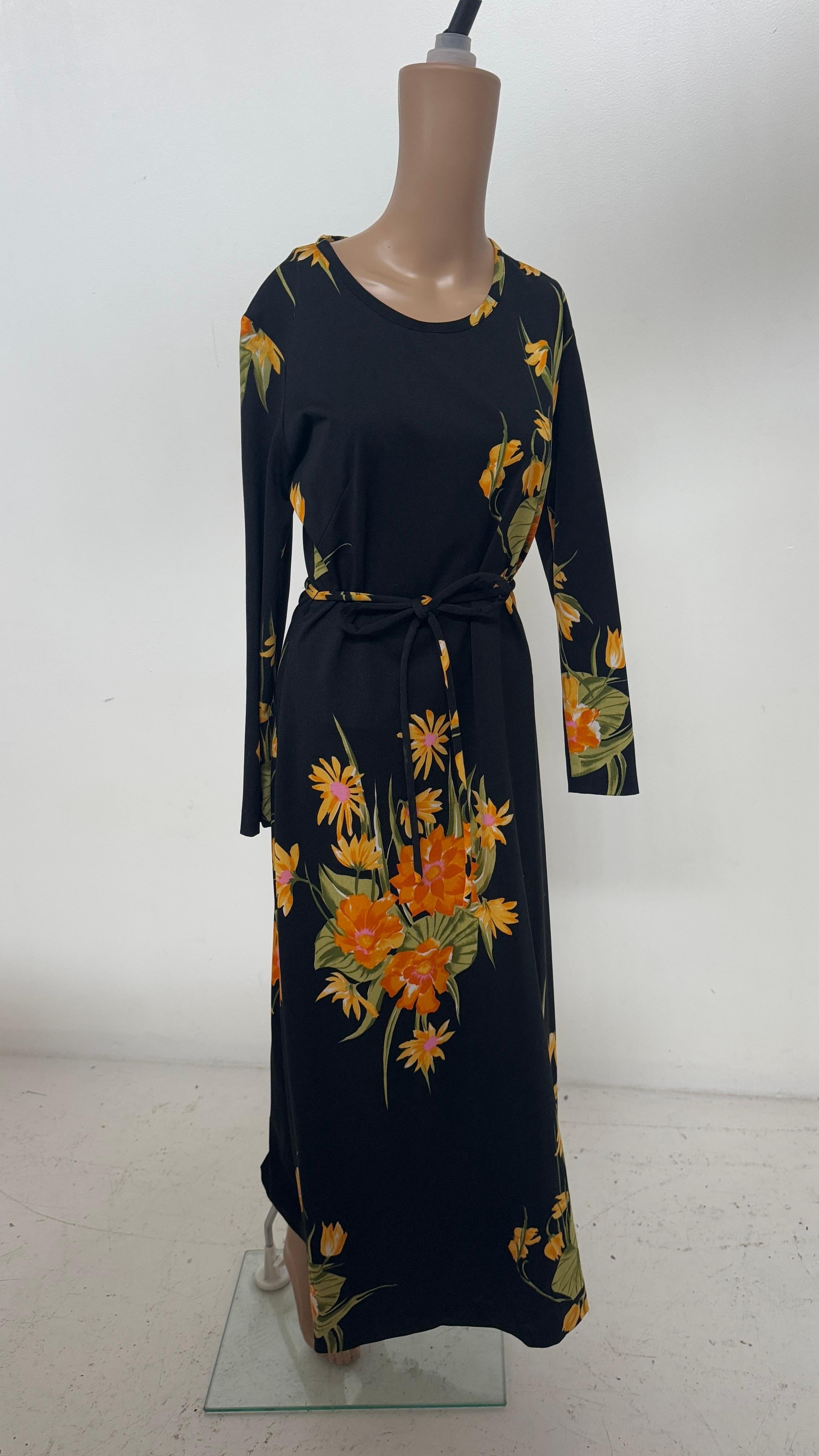 Este maxivestido italiano de los años 90, una vibrante celebración de la feminidad vintage, presenta un llamativo estampado floral integral en ricos tonos naranja, amarillo y verde que resaltan sobre un fondo negro azabache. Confeccionado en viscosa