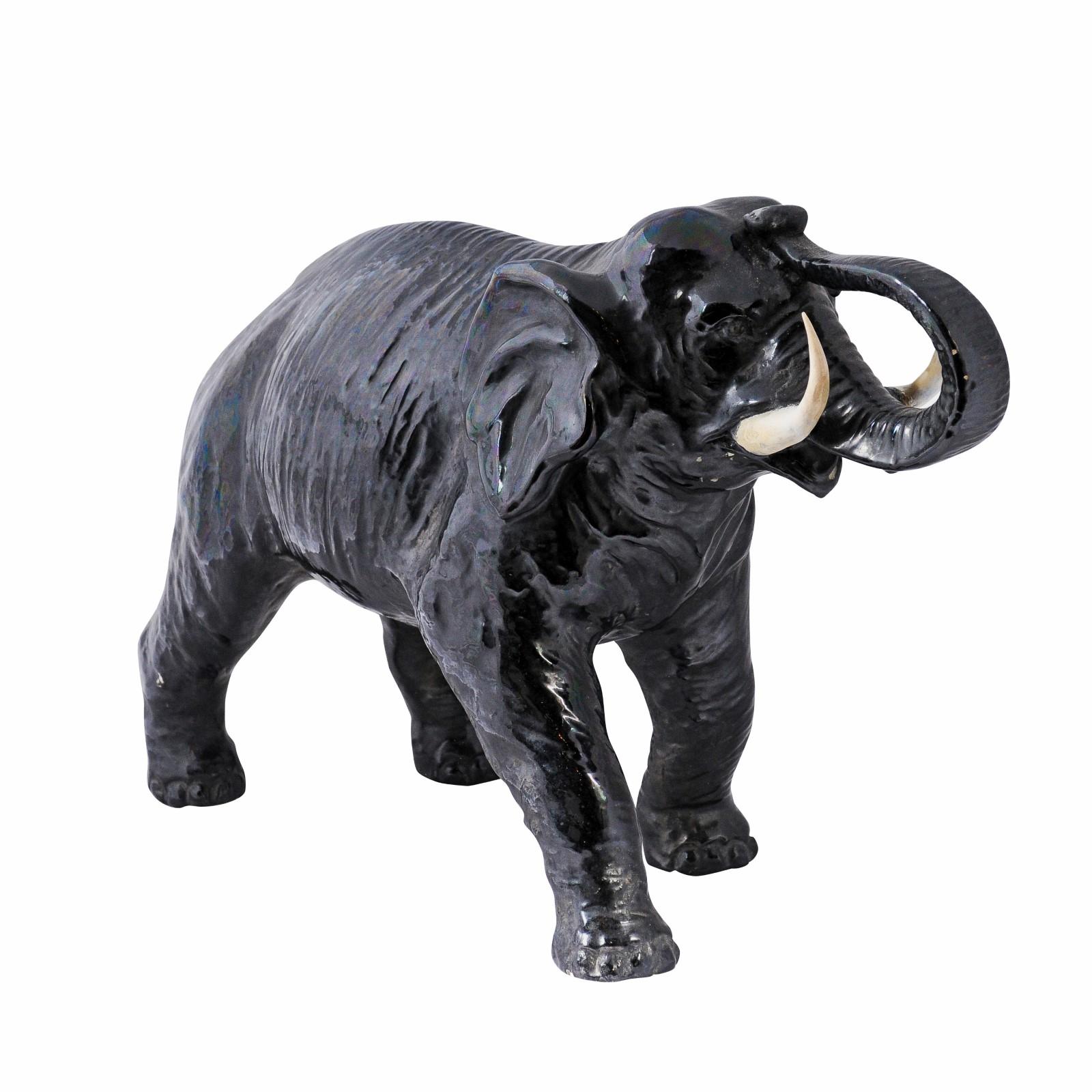 An Italian black glazed ceramic walking elephant from the 20th century with trunk up and glossy finish. Discover a blend of style and symbolism with this Italian black glazed ceramic elephant from the 20th century. This striking piece of art exudes