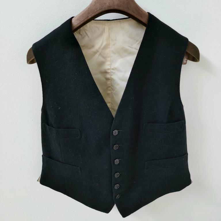 
Vintage Italian black wool tailcoat (“smoking”) with its original waistcoat, bespoke-made in the 1950s for formal daytime occasions. The tailcoat is cut from dense melton wool with steep peak lapels, a single-button cut-away front and curved tails