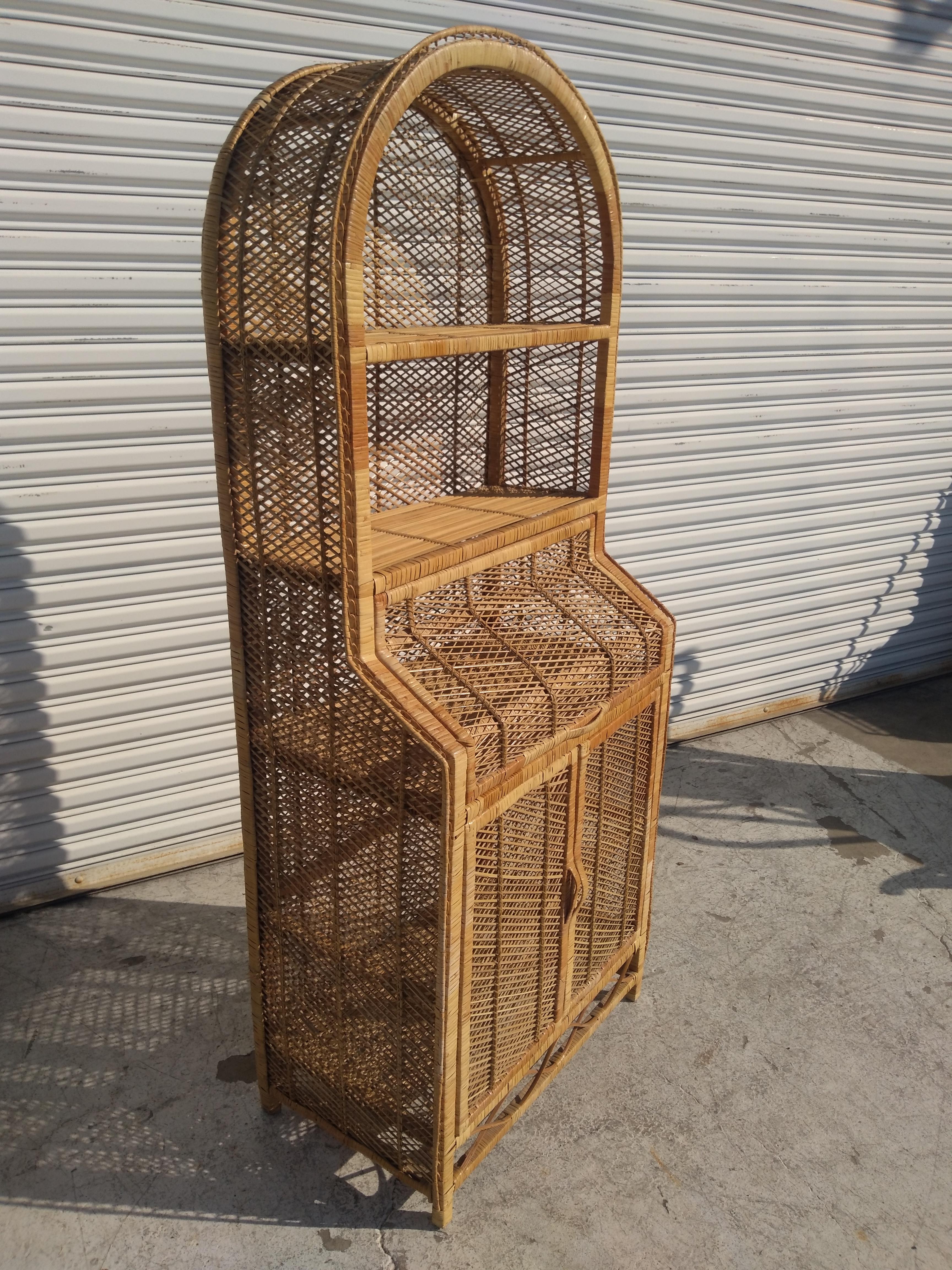 This is a 1970's Boho Chic Bookcase made in Italy. It's made of rattan and bamboo. The top arch has 2 shelves for books. The middle opens up to reveal storage. The bottom has dual doors for even more storage. It's a fine example of Boho Chic