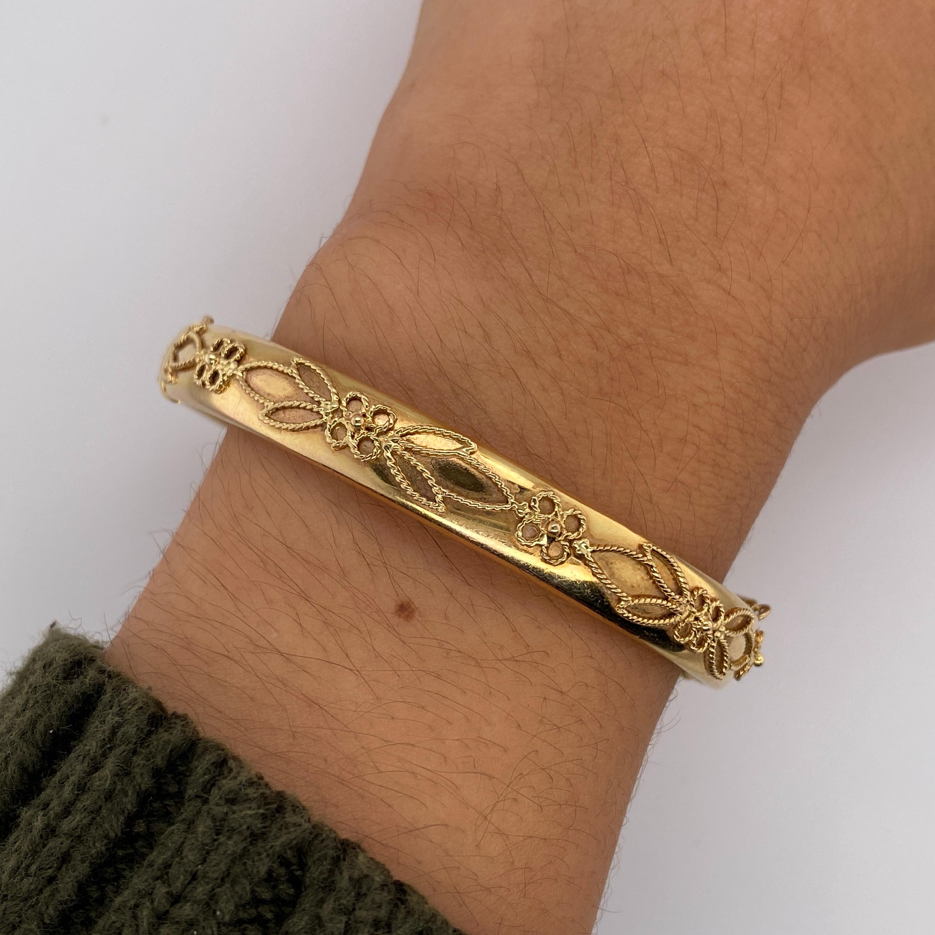 This beautifully preserved vintage Italian bracelet is made in 14 karat yellow gold. The softly reflective surface of the bracelet is decorated in a leaf and flower or clover design made out of twisted wire. The hinged bangle bracelet measures 8