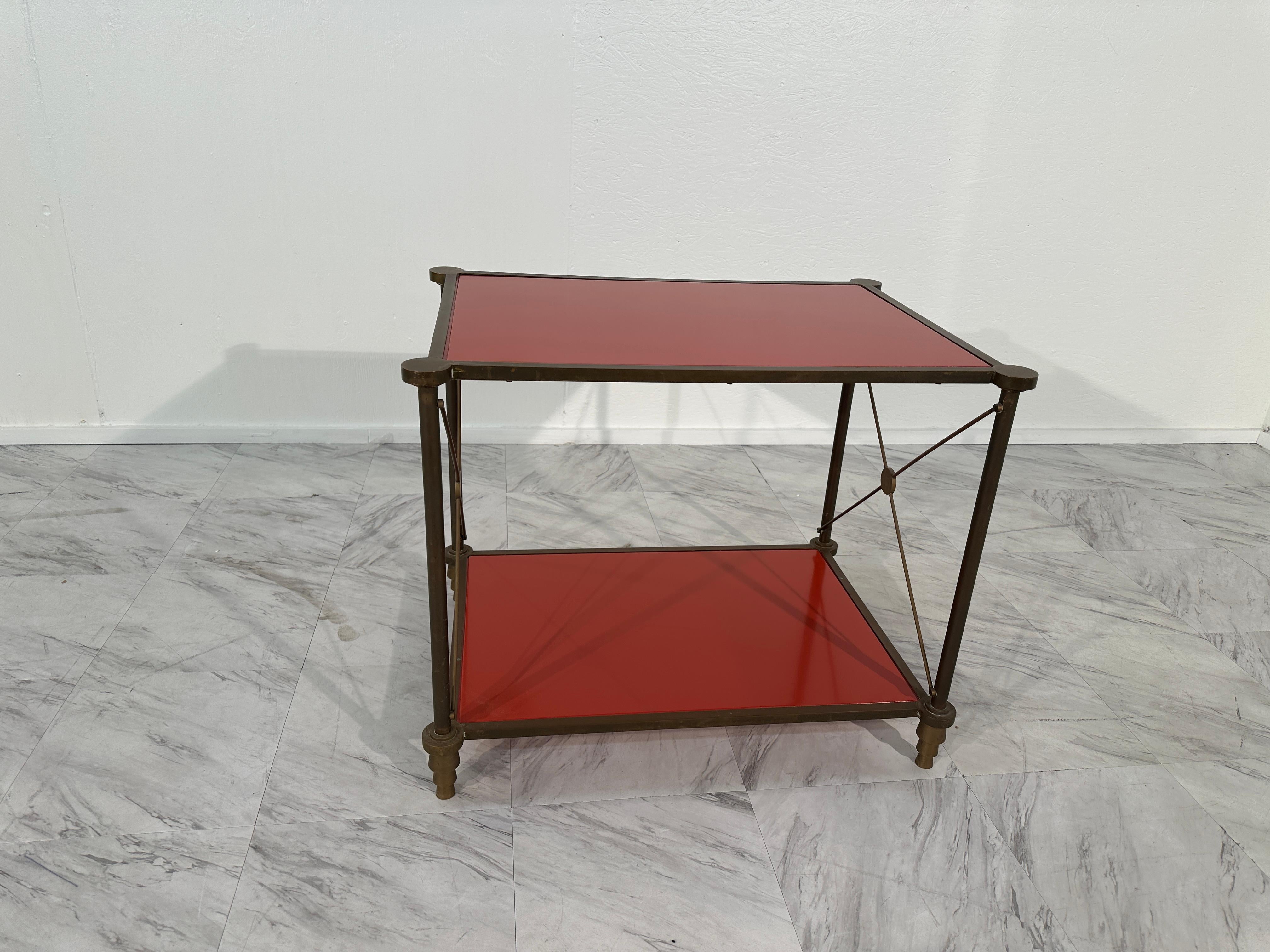 The Vintage Italian Brass Side Table from the 1980s boasts a sleek and sophisticated design, epitomizing the glamour of the era. Crafted with a fully brass frame, this table exudes luxurious charm and durability. Its two red tops add a pop of