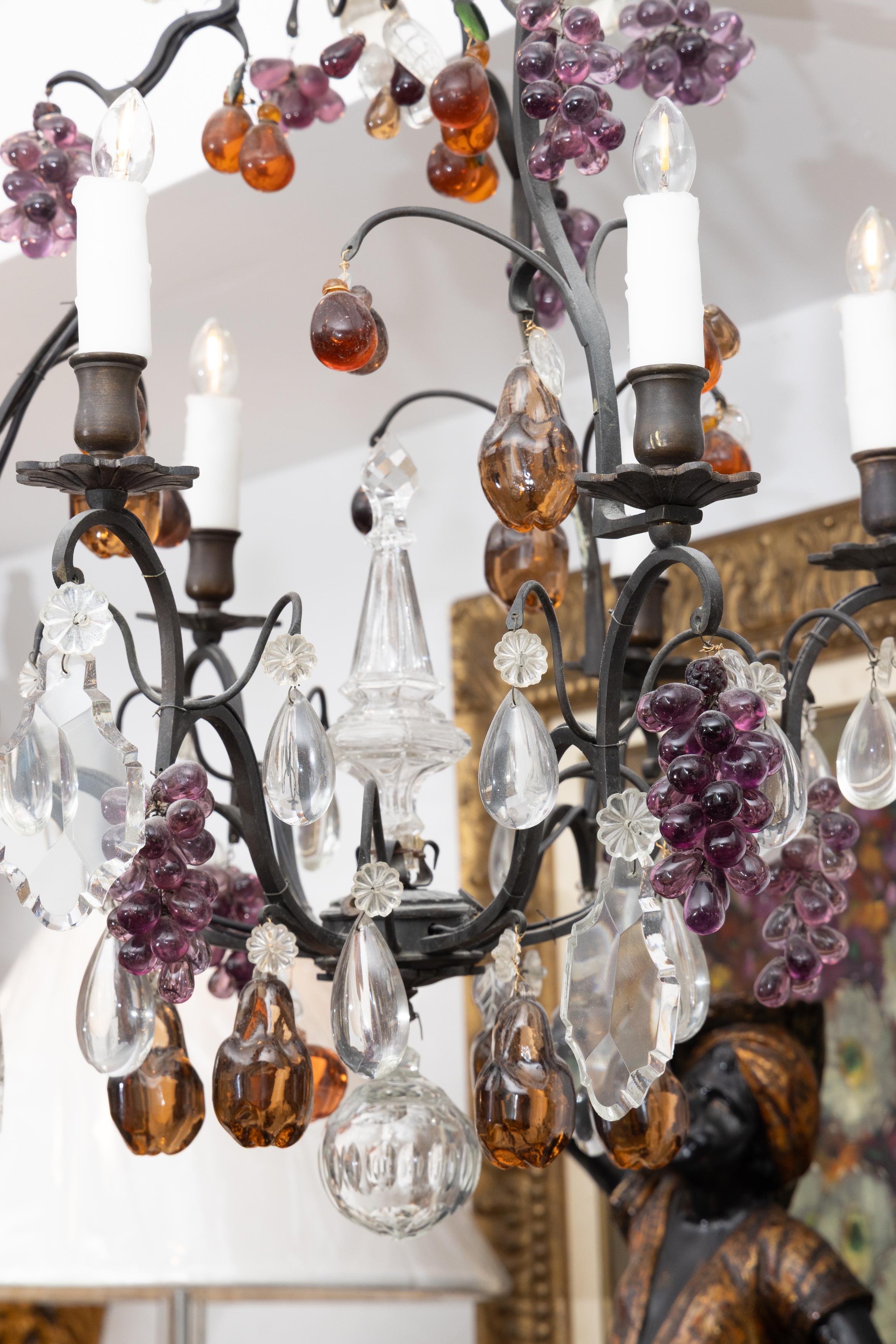 This is a lovely vintage Italian bronzed metal chandelier in bird cage form, bearing clusters of amber and amethyst colored glass fruit displayed in conjunction with shaped crystal pendants.
