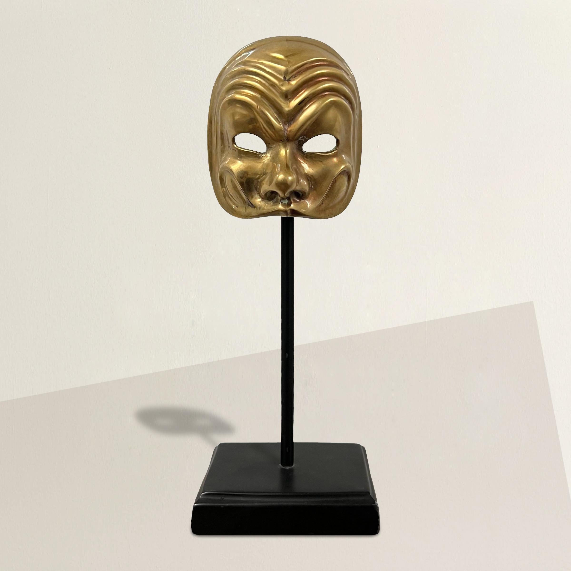 This miniature cast brass Italian opera mask, mounted on a custom steel stand, offers a charming glimpse into the extravagant world of 18th and 19th-century Venetian masquerade balls. Exquisitely detailed, this half-mask, though diminutive in size,