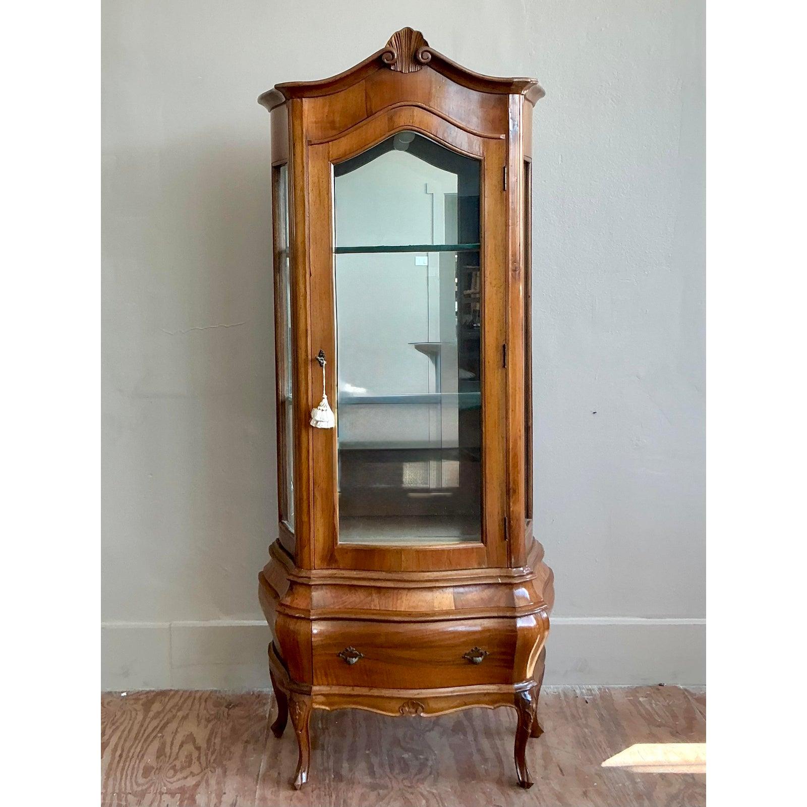 Esempio di artigianato classico italiano, questa splendida vetrina è una testimonianza di eleganza rococò senza tempo. Costruito meticolosamente in legno di radica riccamente scolpito, le sue venature luminose e calde e le sue linee serpeggianti