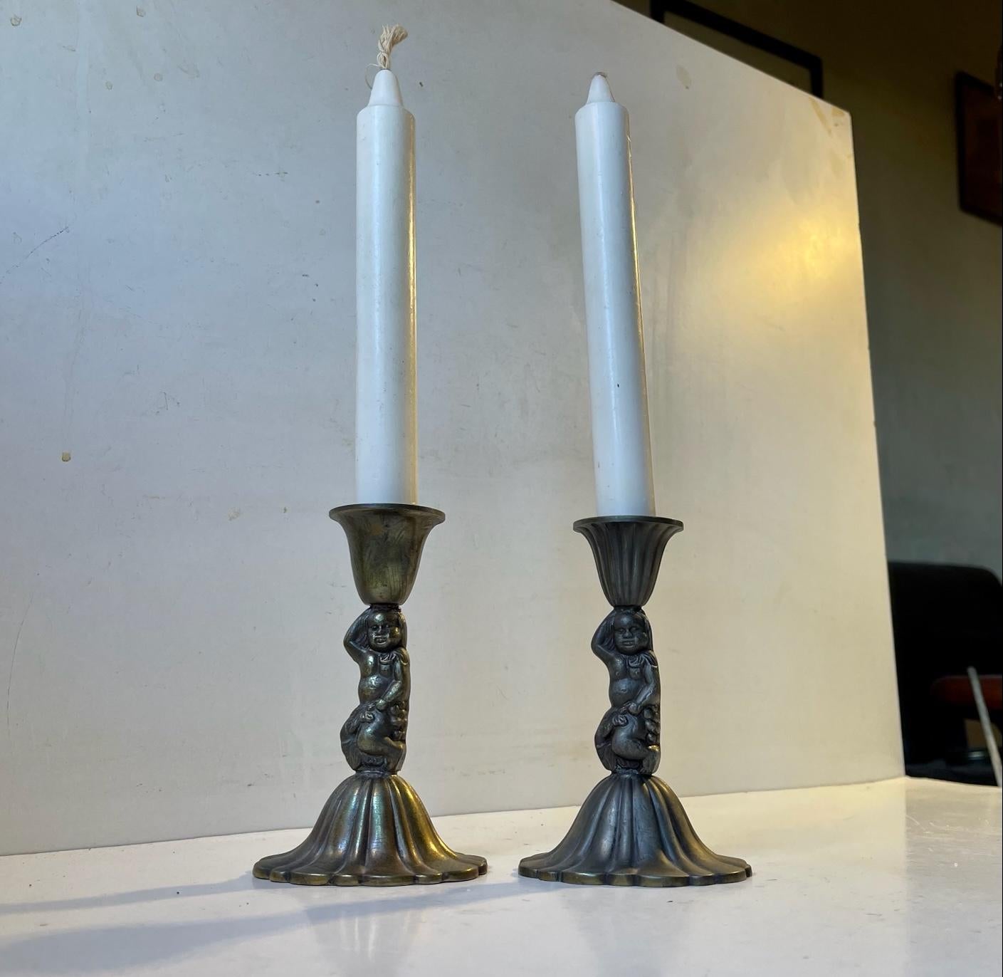 A pair of metal-alloy candlesticks with cherubs. Each one with diffrent patina. Manufactured in Italy during the late 1940s. This set uses regular sized candles. Measurements: H: 13 cm, W: 8 cm (base).