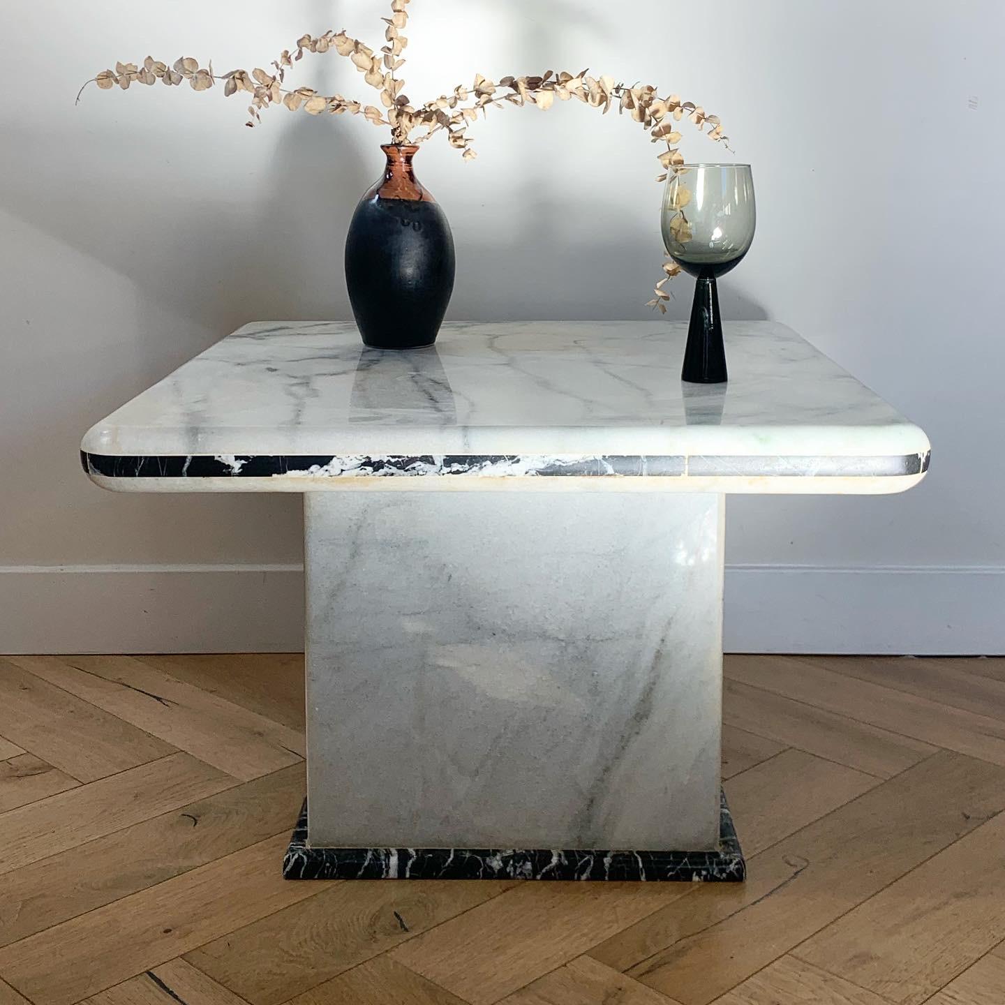 THE FINE PRINT: vintage Italian marble table in ivory carrara with noir marquina accents and edging, 1970s. Ever so slight caramel veining. Top is thick and chiseled into a quarter bevel which reads as bullnose. Pedestal base. Faint and minimal