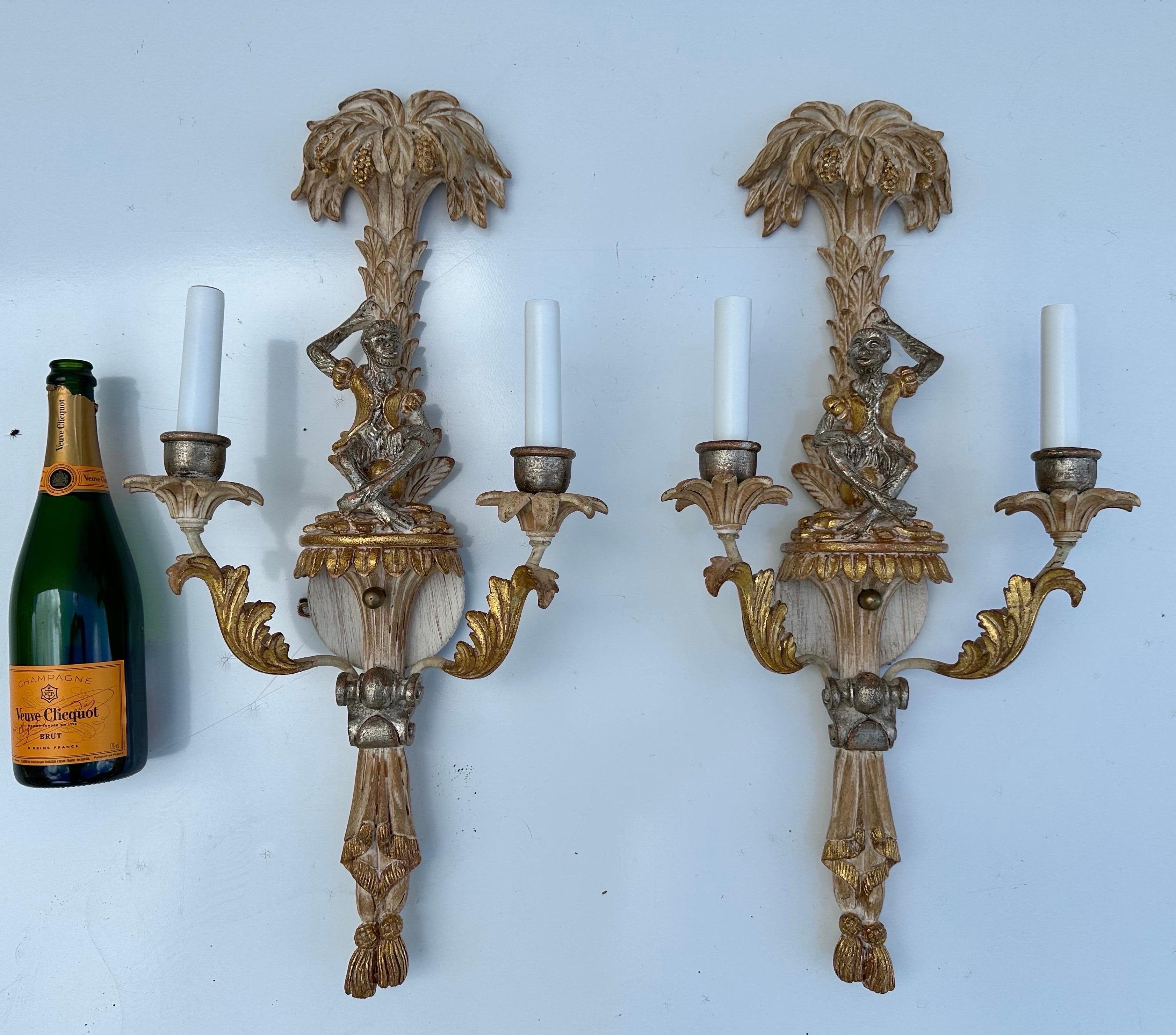 Paire d'appliques à deux branches vintage italiennes sculptées et peintes, représentant un singe assis sur un ballon portant de l'or  Veste colorée, reposant sous un bananier blanc avec des grappes et des feuilles de bananier, sur un piédestal
