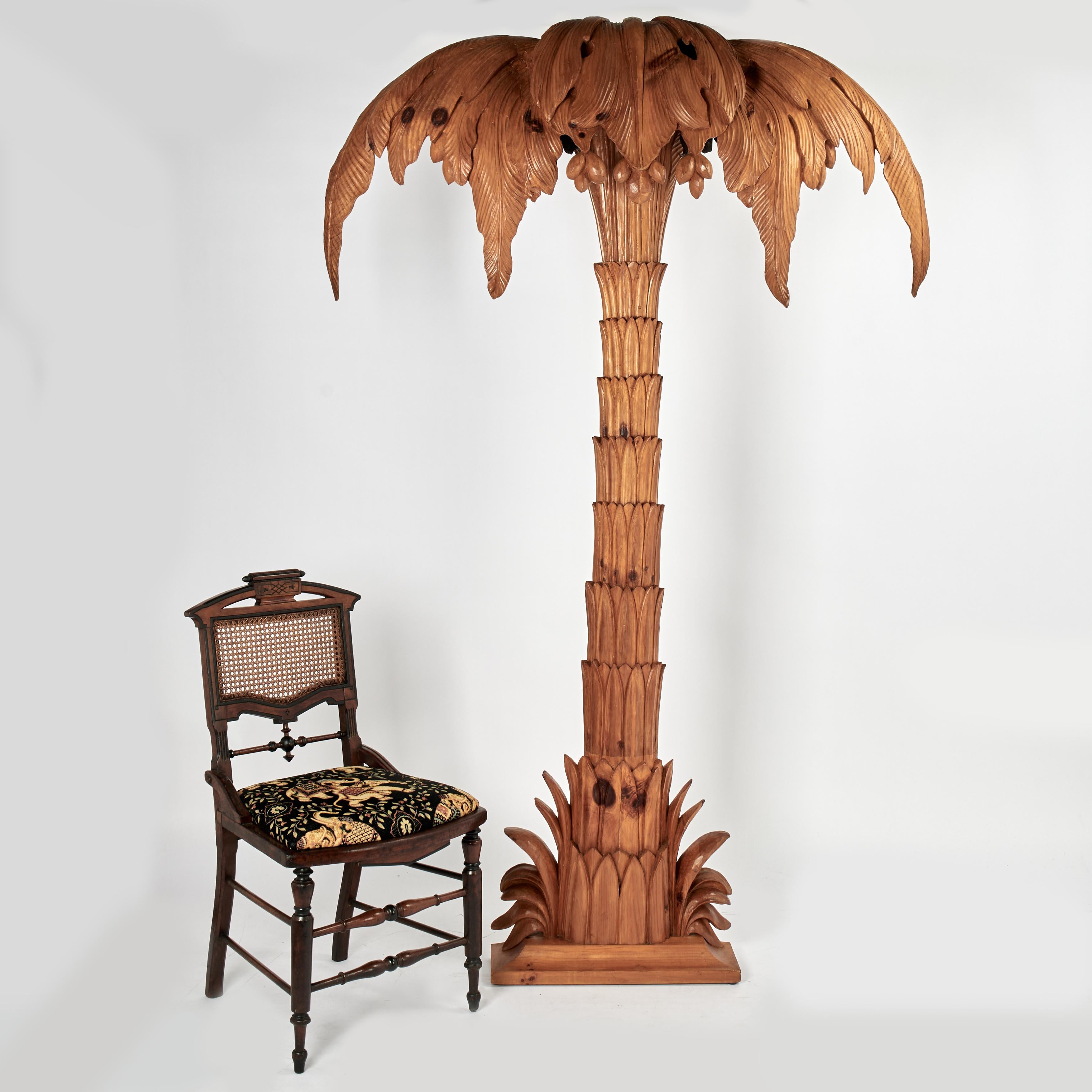 Elegante lampada da terra a parete italiana della metà del secolo scolpita a mano in pino duro con una forma di palma stilizzata con foglie e noci di cocco retroilluminate su un tronco stilizzato e una base smussata con foglie.