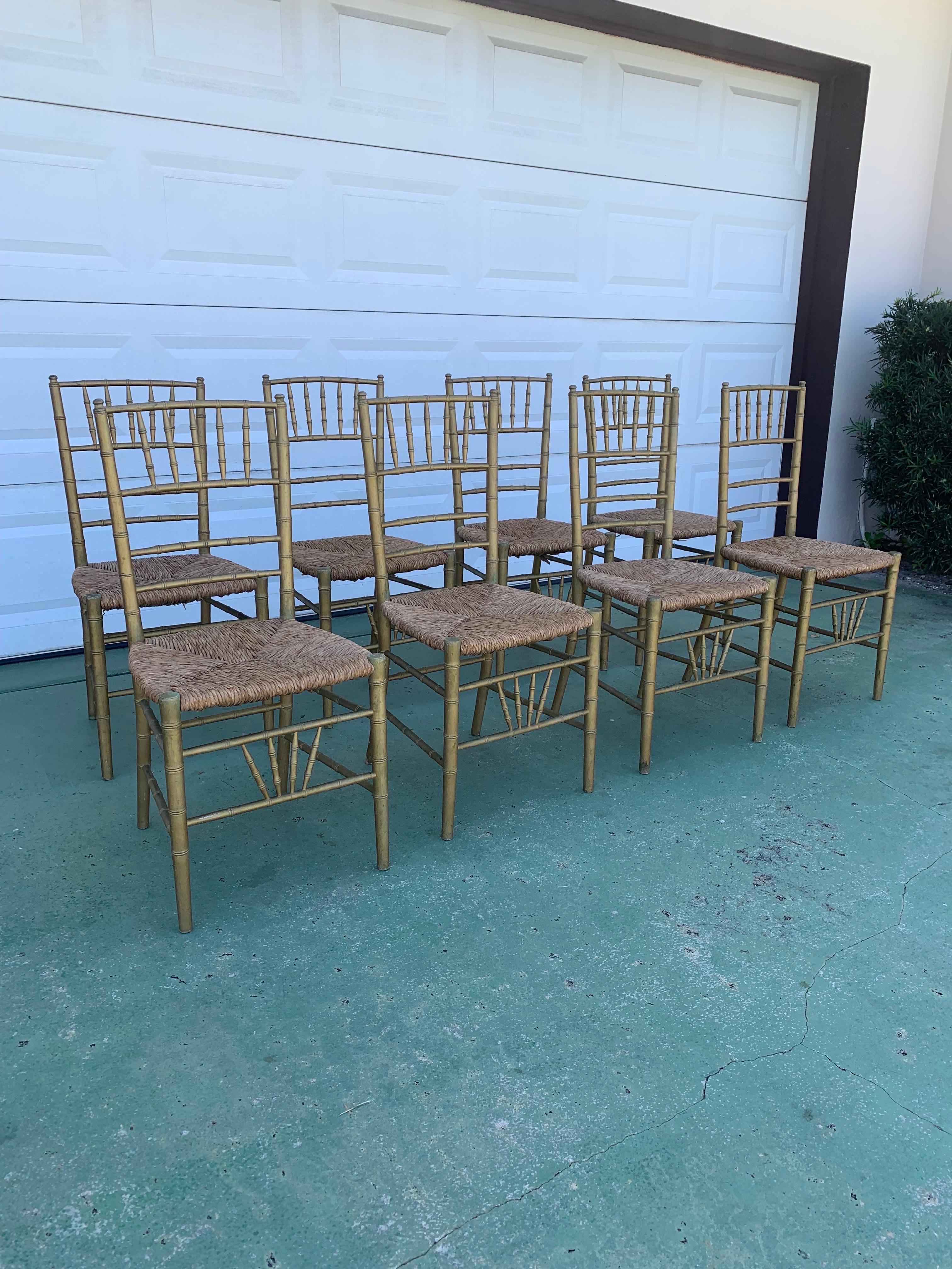 A beautifully aged set of 8 Italian Chiavari style dining chairs. Carved wood to mimic bamboo and gilt paint that has a great look of wear and age. Rush seats and custom made cushions. These chairs have a Classic look and are still copied cheaply to