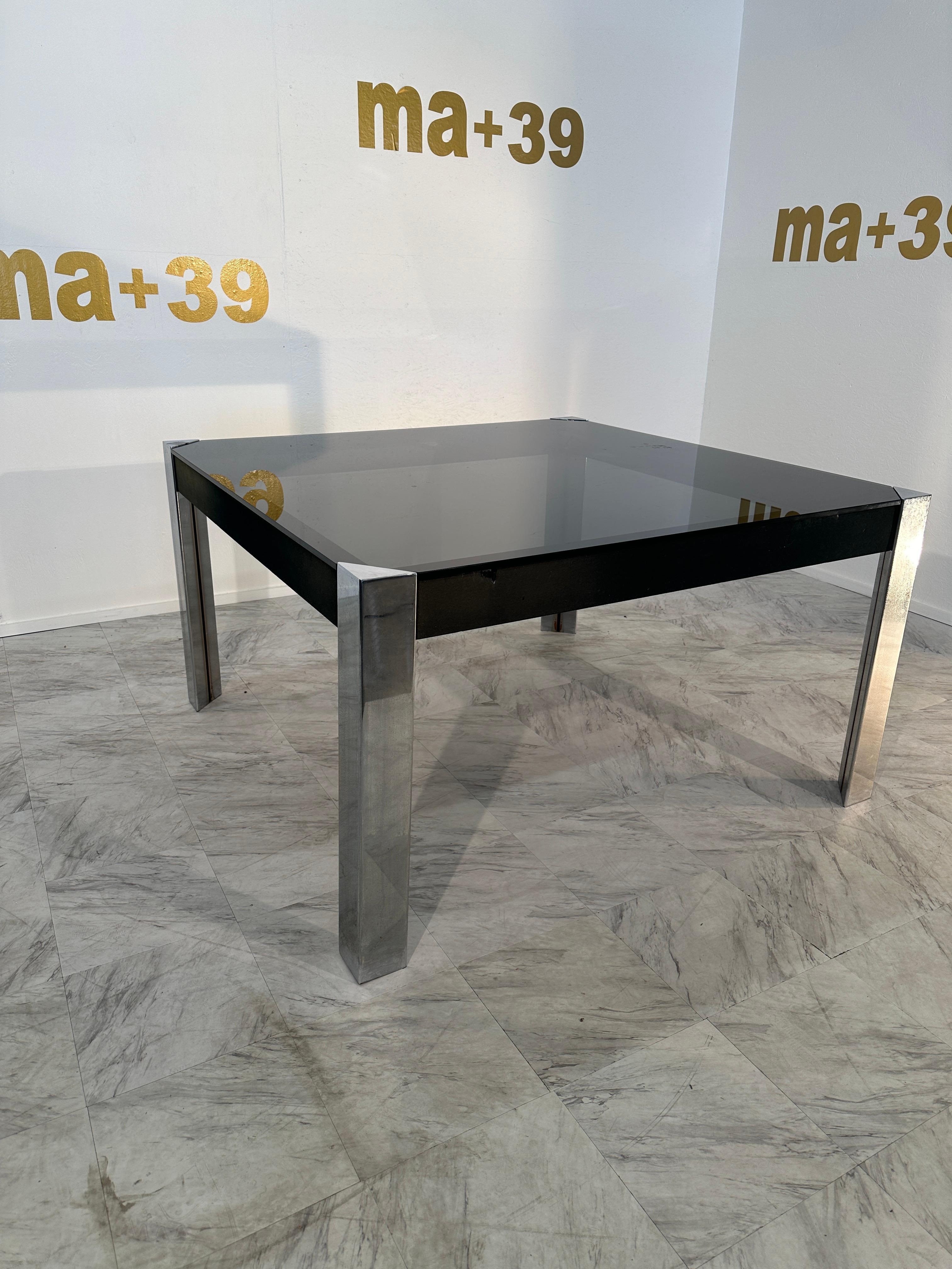 The Vintage Italian Chrome and Glass Dining Table by Guido Faleschini X Hermes features a distinctive design with a chrome base and an obscured black glass top. This piece reflects a blend of Italian craftsmanship and luxury, showcasing a stylish