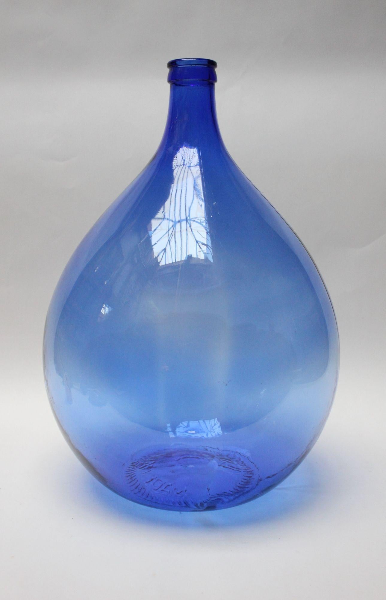 Large 54-liter demijohn / carboy in uncommon cobalt blue glass originally used for transporting wine (ca. mid-20th century, Italy).
There is a cluster of small scratches to the neck, as shown, along with light, general wear consistent with