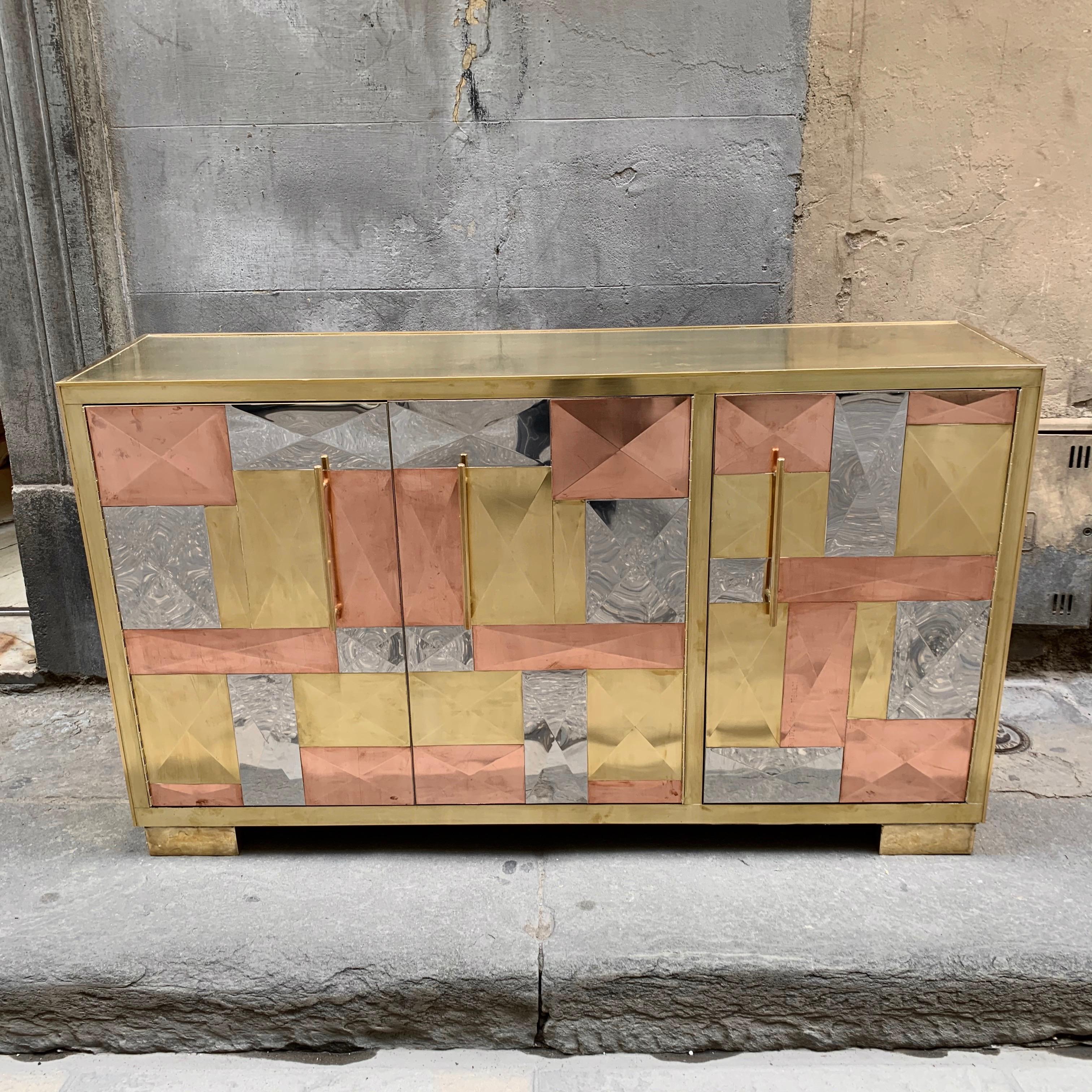 Vintage Italian credenza with brass, copper and steel plates with geometric design.
The top of the furniture, the handles and the legs are made of brass. The sides and the three front doors are made of mosaic pieces of brass, copper and steel