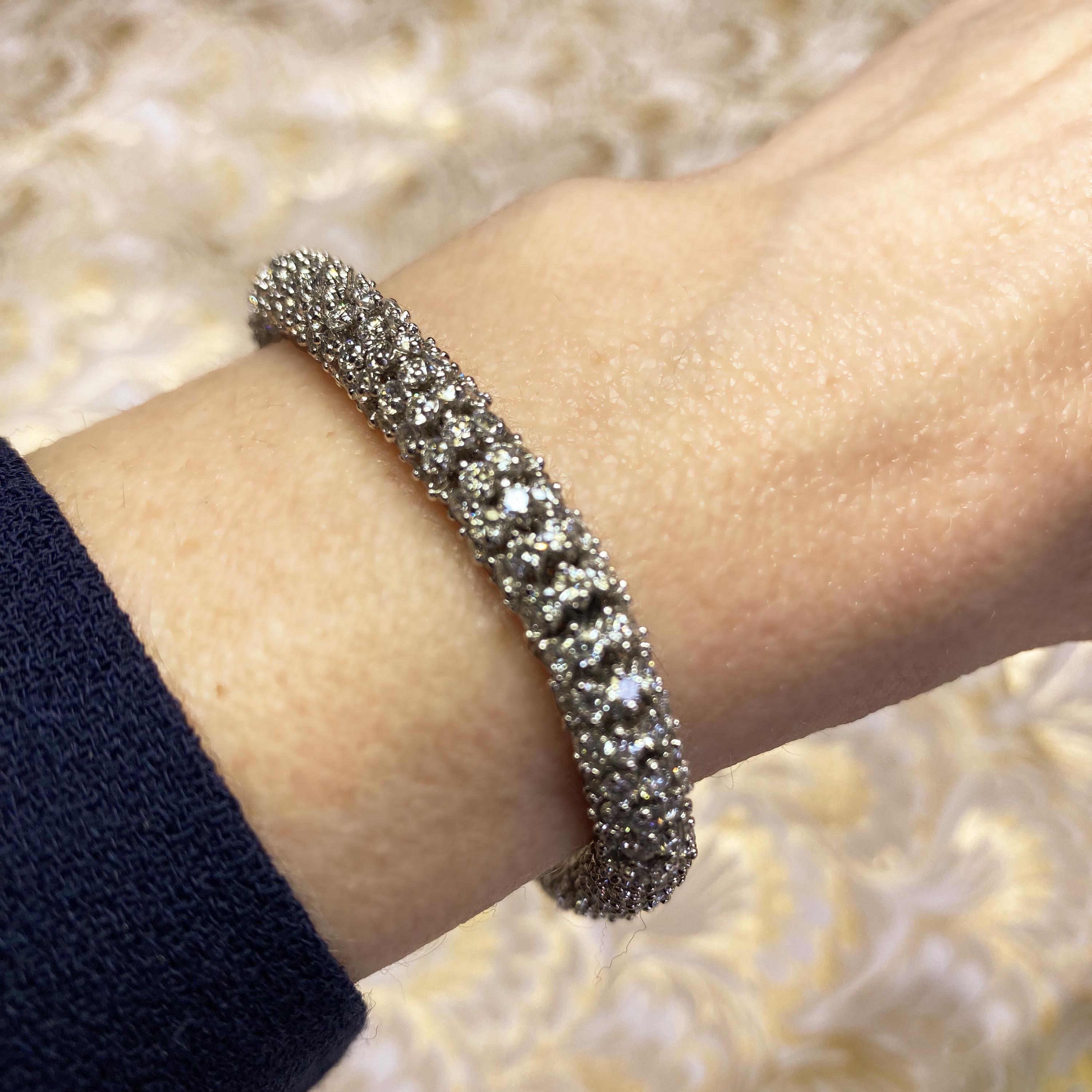 A vintage diamond bracelet of rondelles, each set with eight round brilliant-cut diamonds, in claw settings, linked together to form an articulated diamond tube, mounted in 18ct white gold, with a box and tongue clasp, with a black enamelled button,