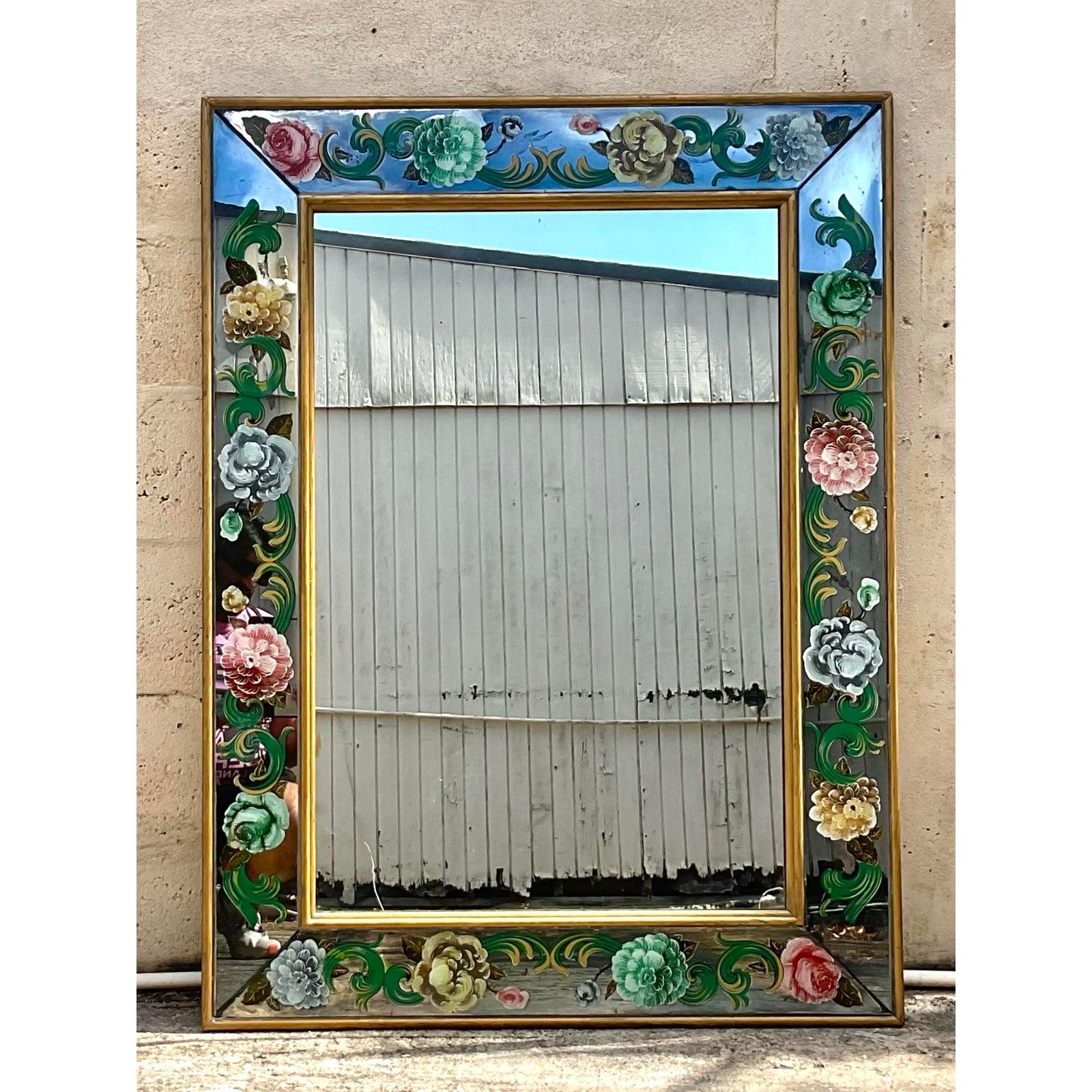 Cette pièce étonnante présente l'art sophistiqué de la peinture inversée et de la dorure sur verre, mettant en valeur de délicats motifs floraux qui s'épanouissent avec des couleurs et des détails complexes autour de sa surface réfléchissante. La