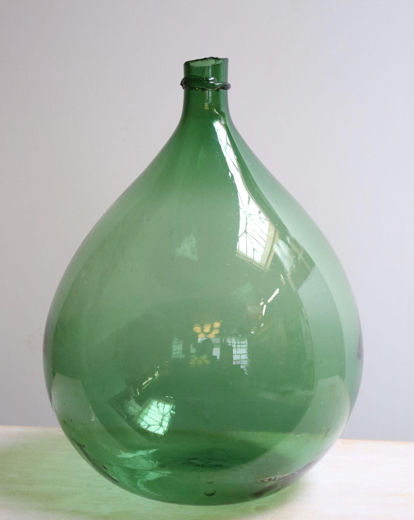 Italian Demijohn / Carboy originally used for transporting wine (ca. early 20th Century, Italy).
Bulbous ballon/teardrop form composed of attractive emerald green free-blown glass exhibiting trapped air bubbles within the glass itself with squat