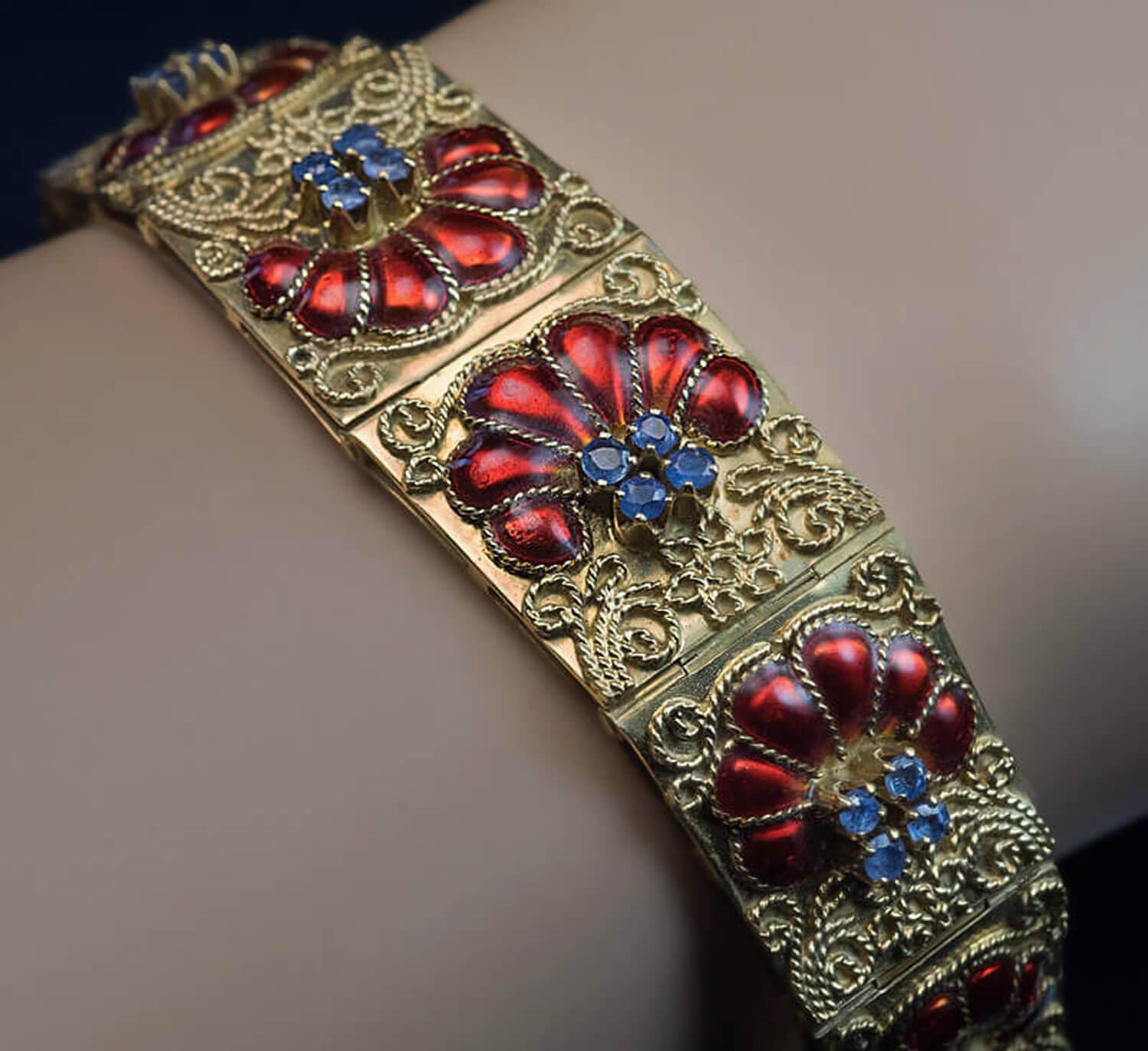 This spectacular 18K gold bracelet was handcrafted in Italy in the 1950s.  The bracelet is embellished with red enamel stylized shells, small blue sapphires and gold filigree.  Weight is 39.35 grams.  Width is 18 mm (11/16 in.)  Length is 188 mm (7