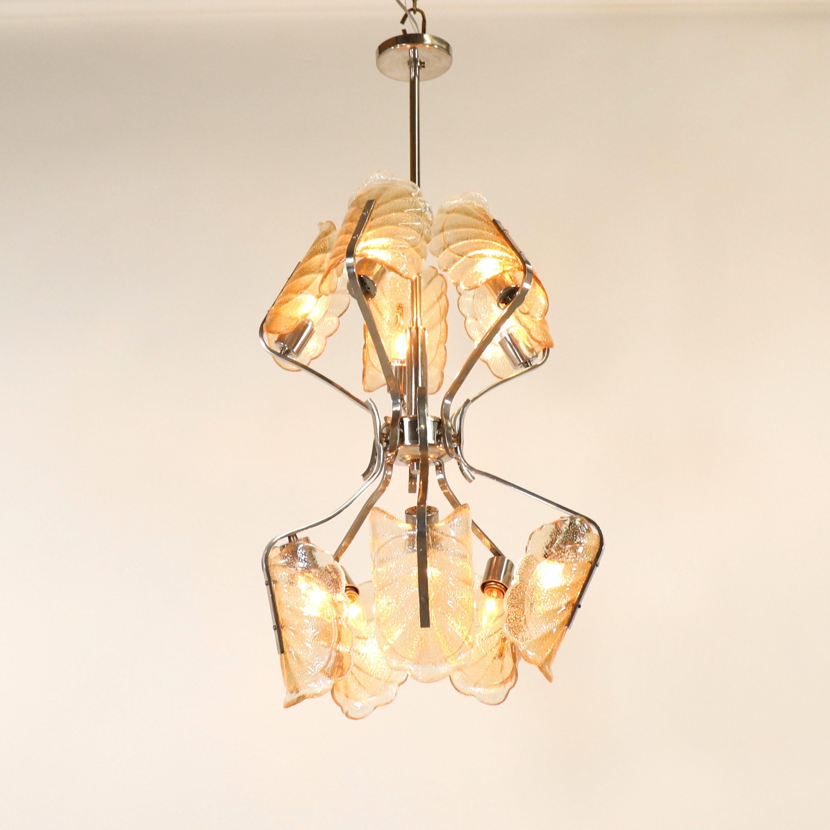 This fascinating mid-century modern two-tier Italian glass chandelier features acanthus leaf shades on a chrome frame. The textured glass shades are enhanced with amber specks dispersed throughout and concentrated on the trim, creating a lush orange
