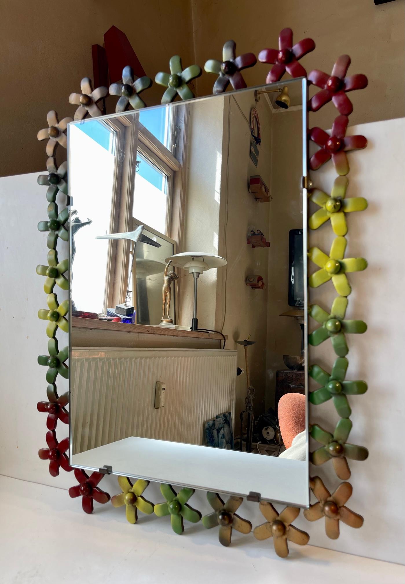 A very heavy sculptural wall mirror in welded iron. The frame is set with multi-colored flowers. Bought at a Flea marked in Verona Italy and made during the 1970s locally. Measurements: H: 63/49 cm, W: 47/35 cm, Dept: 3 cm.