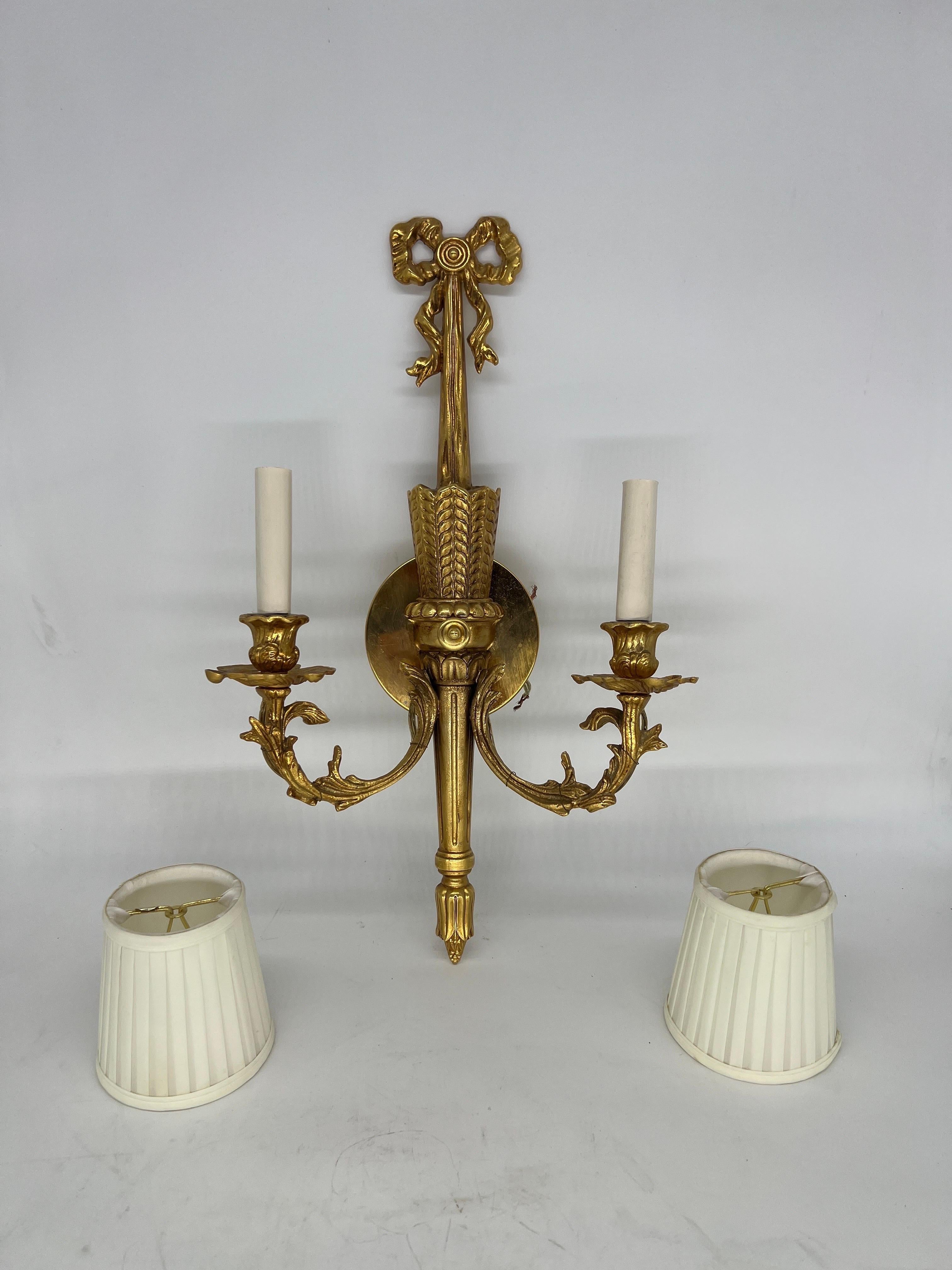 Italian, 20th century.

Each of these sconces have a gilt bronze body in a traditional neoclassical or adams style form. They feature a two arm design with professional wiring. Also included with each sconce is a pair of shades. Marked to verso