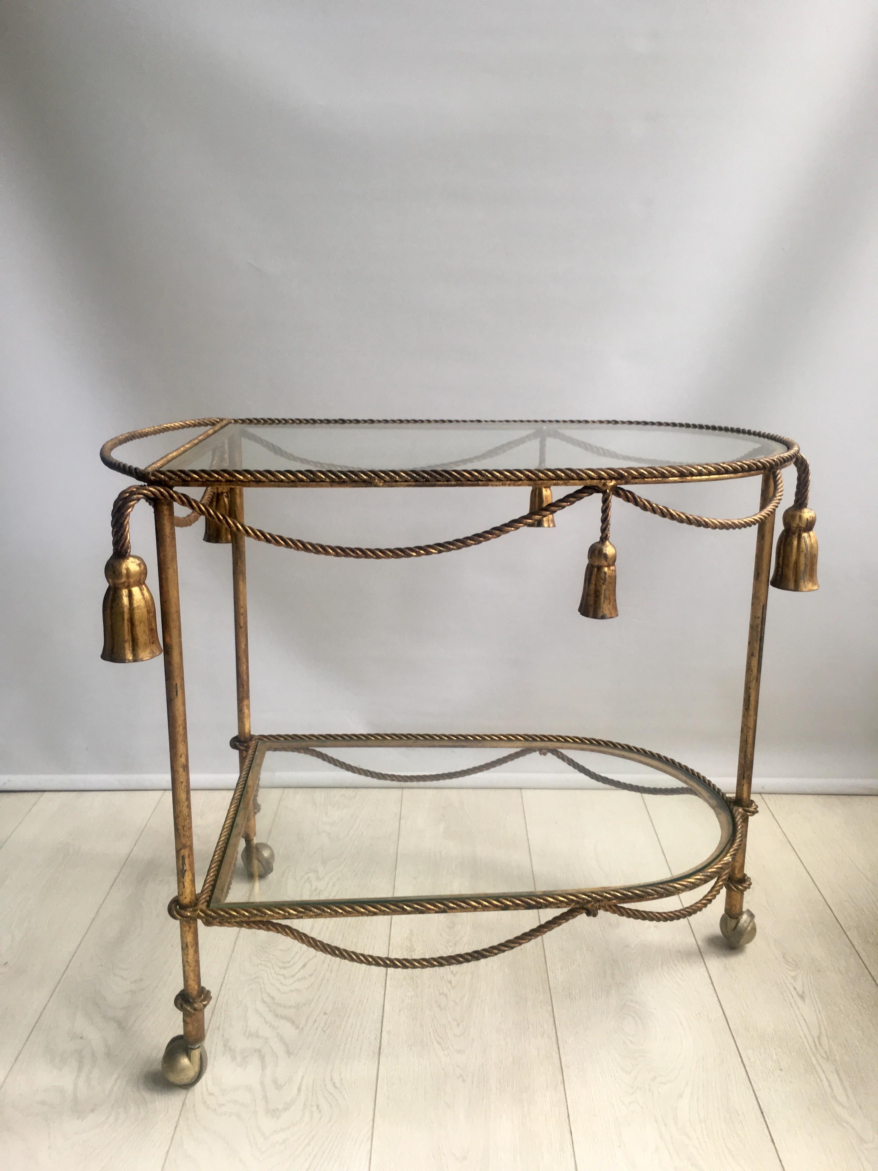 Not for wall flowers, this fabulous Italian midcentury Hollywood Regency gilt-tole drinks trolley with gold twisted rope and tassel details.

Lovely coloring to the gilt metal frame, some signs of wear as per close up images.

Top tray measures