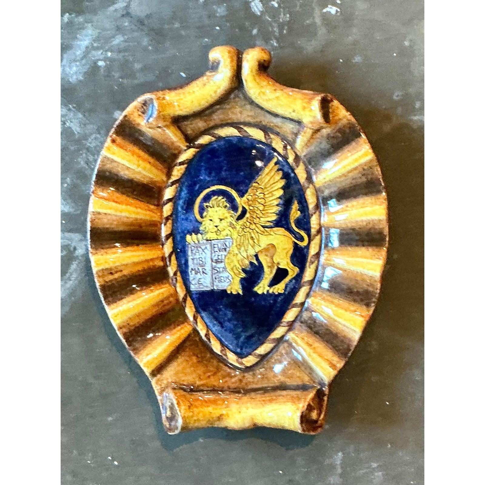Dieses exquisite Wappen aus glasierter italienischer Vintage-Keramik mit dem geflügelten Löwen ist ein wahrhaft fesselndes Fundstück, das eine reiche Geschichte und Kunstfertigkeit verkörpert. Diese mit viel Liebe zum Detail gefertigte Wappentafel